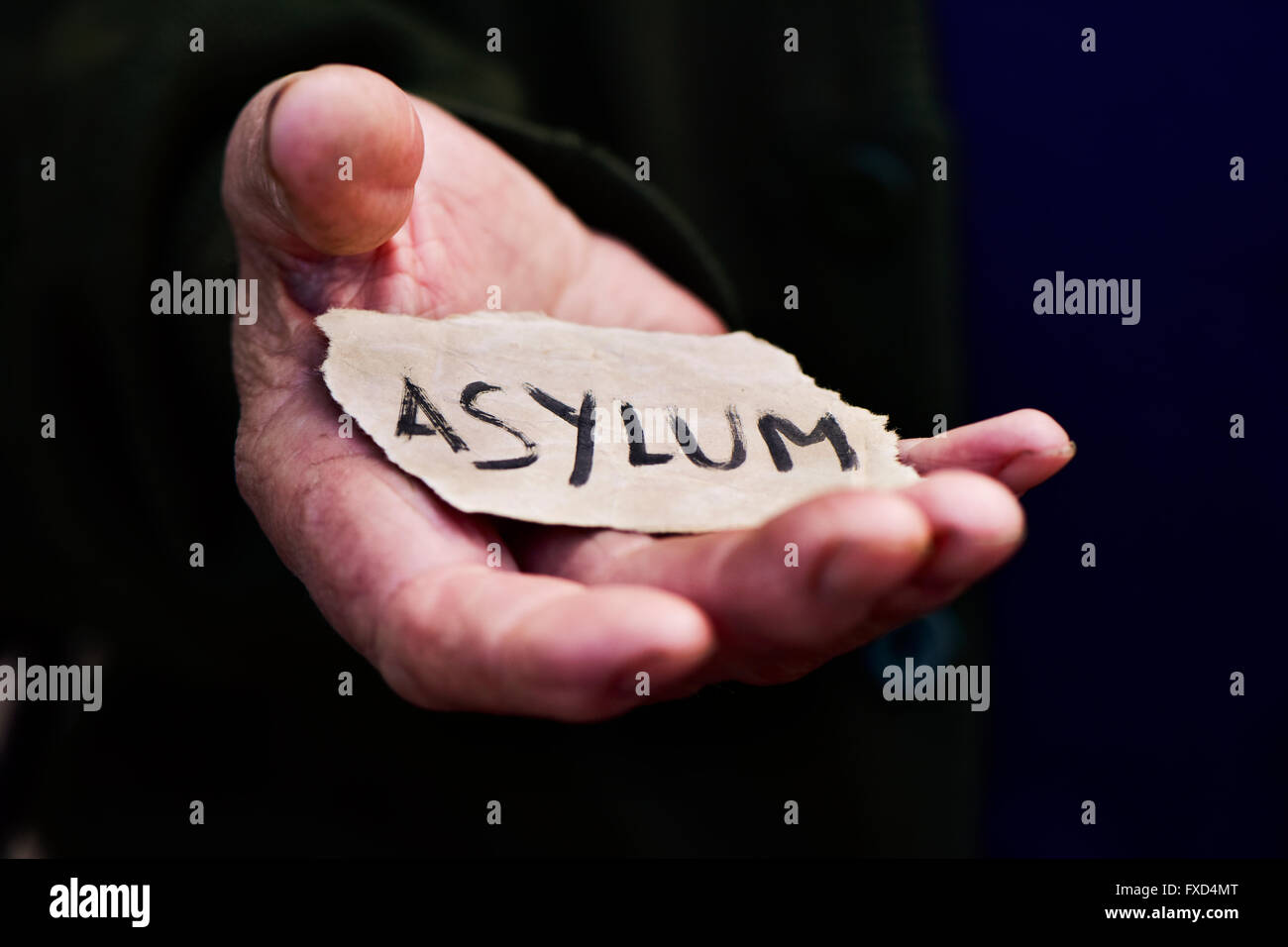 Nahaufnahme der Hand eines alten Mannes mit einem Stück Papier mit dem Wort Asyl, mit einen dramatischen Effekt Stockfoto
