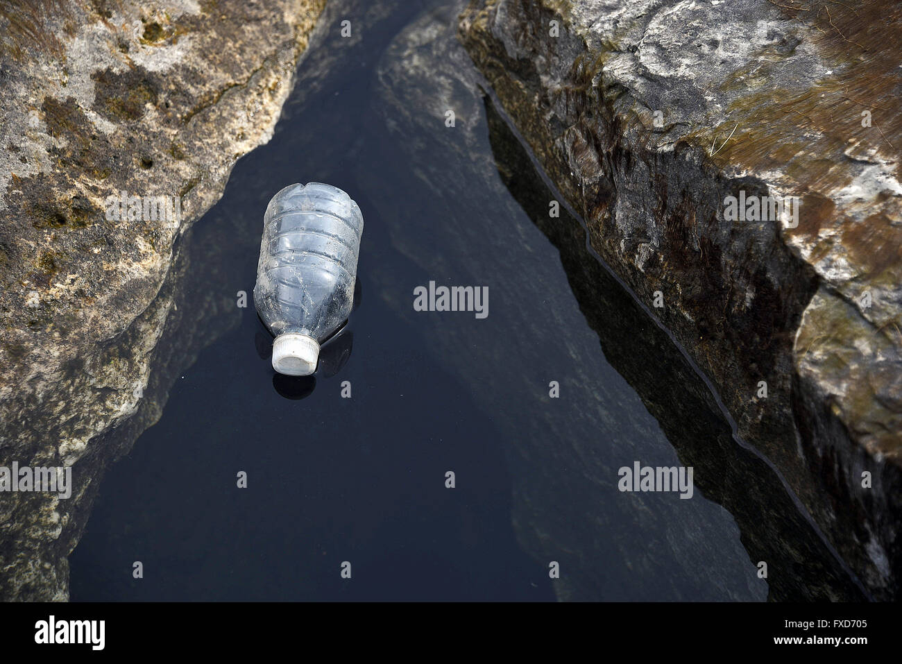 Leere Plastikflasche Wasser schweben im Wasser des Sees zwischen Felsen verworfen. Stockfoto