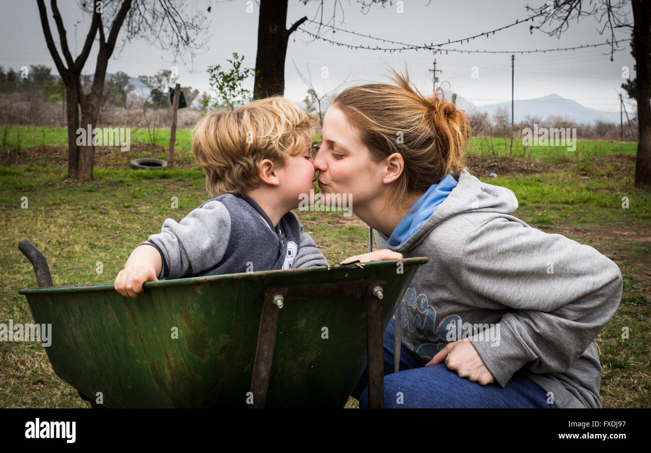 Mutter, küssen ihr junge Kind sitzen in Schubkarre Stockfoto