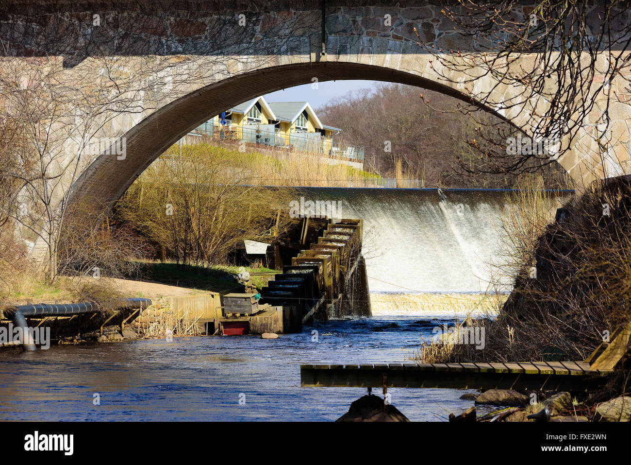 Überlauf mit Streaming-Wasser und eine Holzleiter Fisch gesehen durch die übergreifende Öffnung unter der steinernen Brücke in Lyckeby, Schweden. Stockfoto