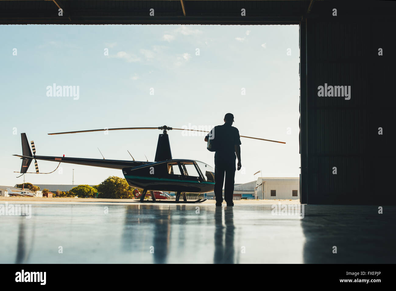 Sicht nach hinten gedreht der pilot zu Fuß in Richtung Hubschrauber. Pilot und Hubschrauber in einem Flugzeughangar. Stockfoto