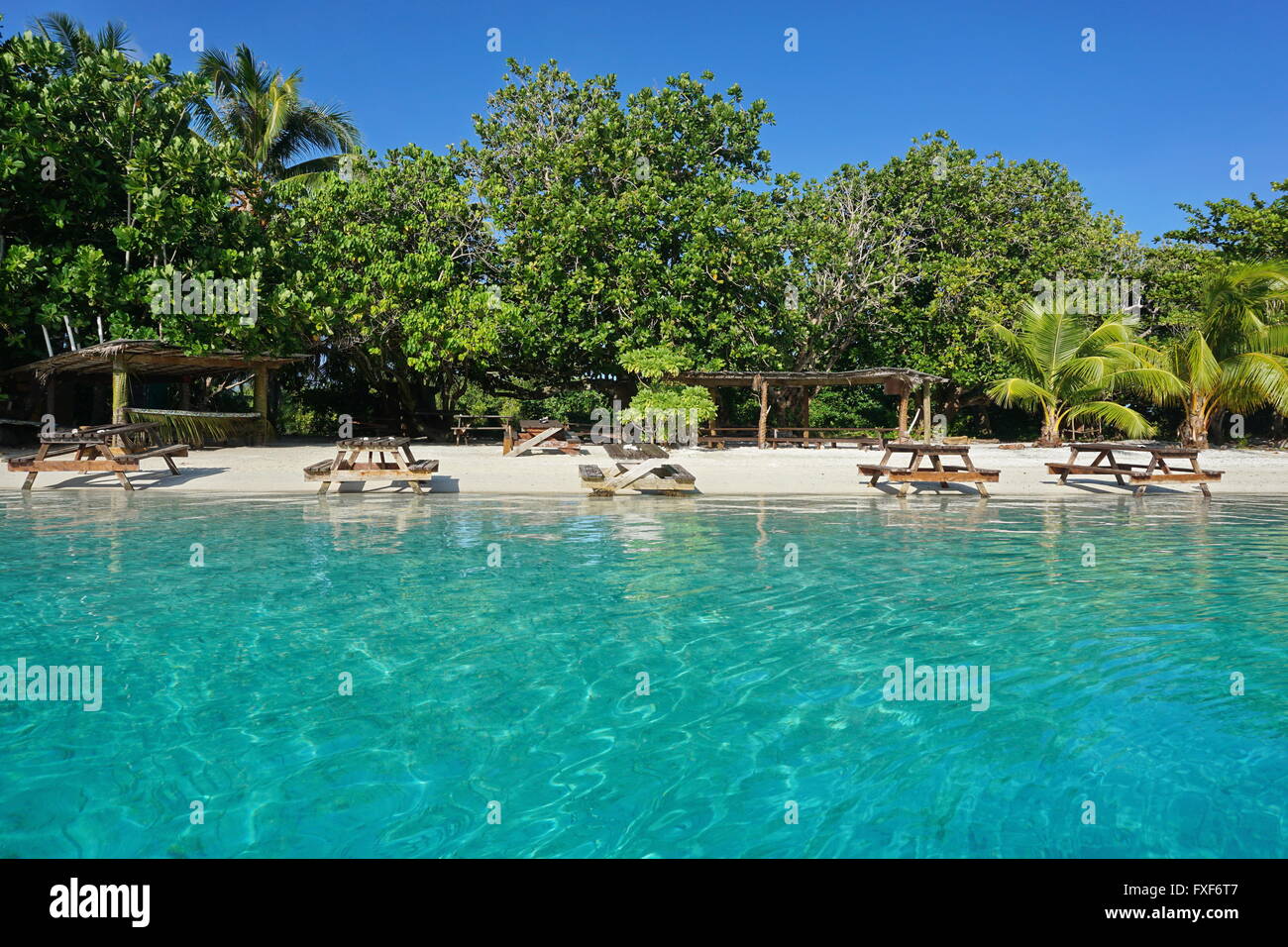 Picknick-Tische an einem tropischen Strand mit türkisblauem Wasser an der Küste einer kleinen Insel, Insel Huahine, Französisch-Polynesien Stockfoto