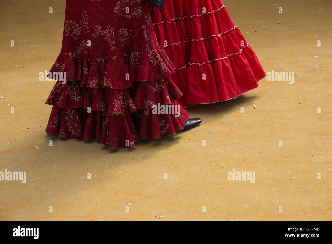 Zwei Damen rote Kleider gegen den goldenen Sand, der auf den Boden an der Feria de Abril (April Fair) de Sevilla in Sevilla, Spanien Stockfoto