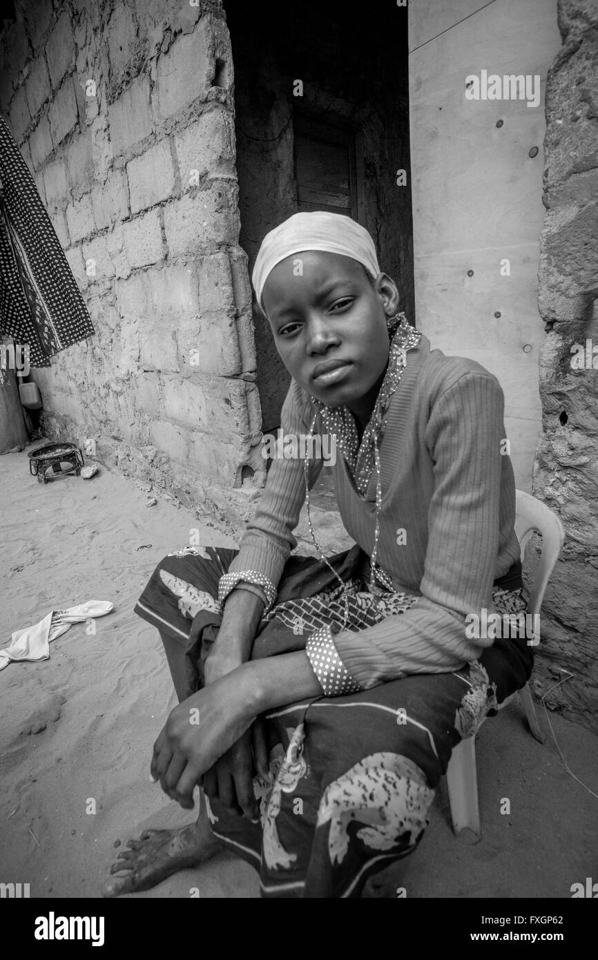 Mosambik, ein Porträt einer melancholischen Frau in traditioneller Kleidung, sitzen auf einem Stuhl vor ihr Haus, schwarz und weiß. Stockfoto