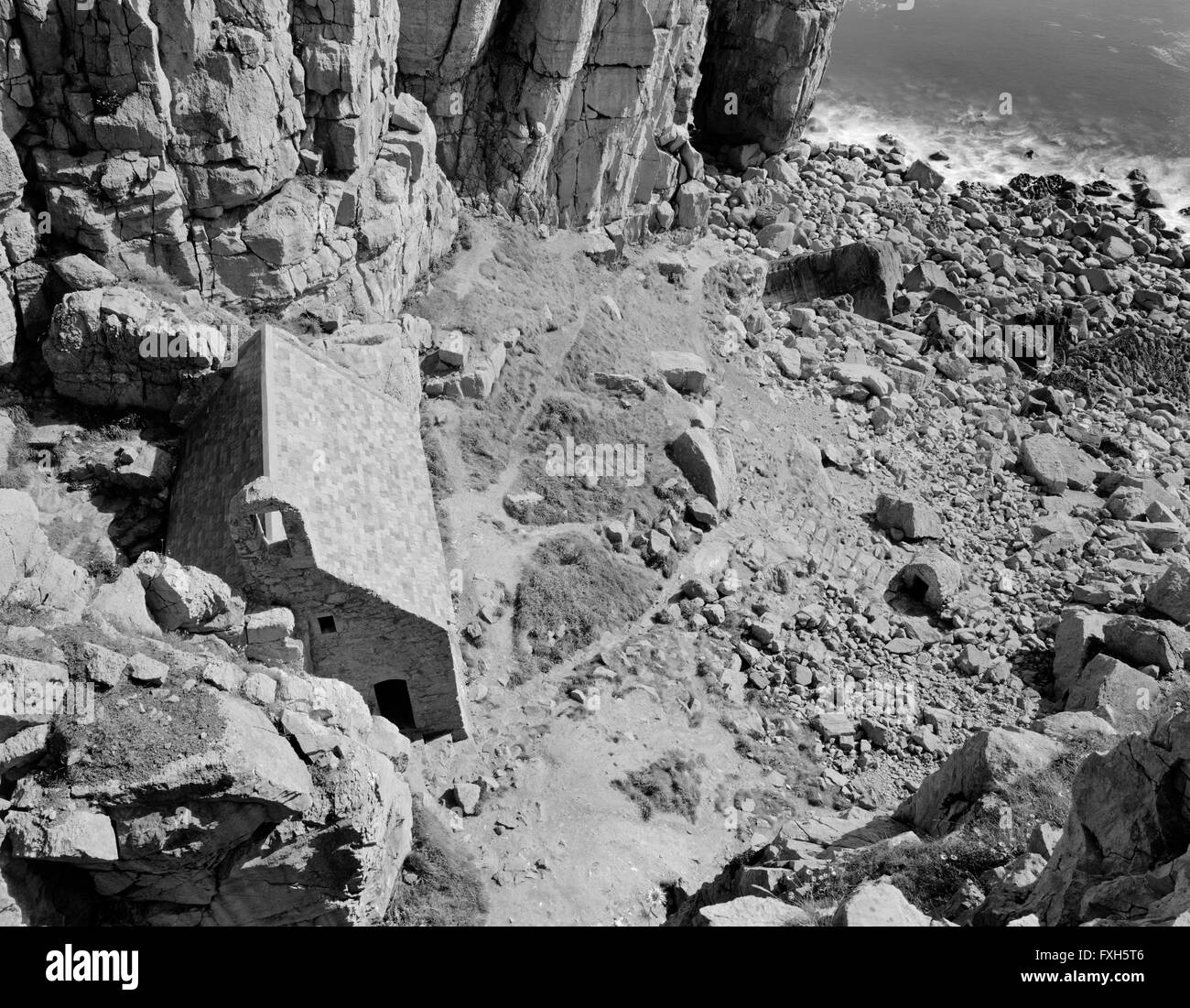 Kapelle St. Govan, Pembrokeshire, schmiegt sich an die Bell Rock (hinten L) unter den steilen Klippen: Stufen führen hinunter zu seinem früheren Heilbrunnen. Stockfoto