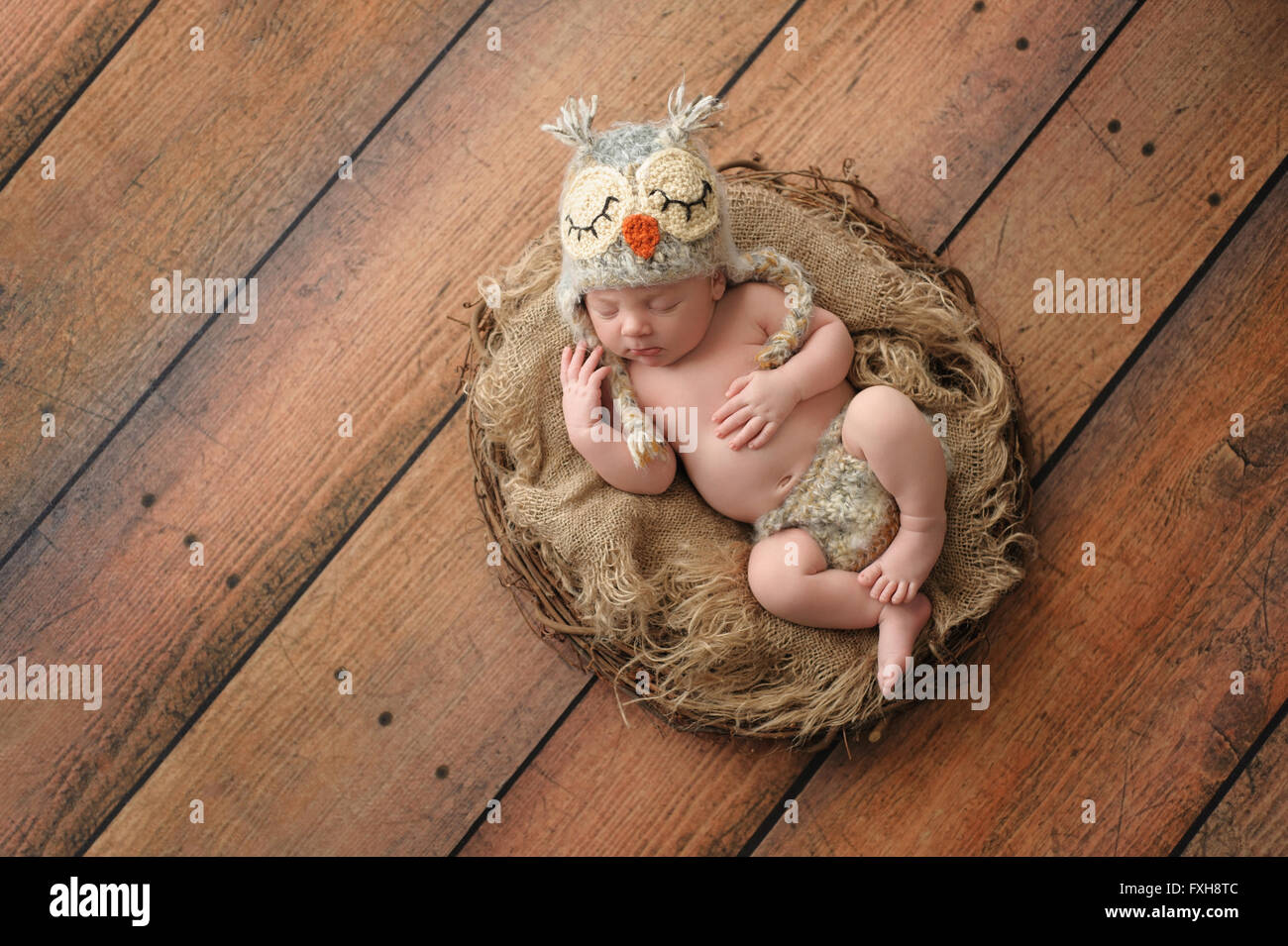 Zwei Wochen altes neugeborenes Baby Boy decken einen gehäkelten Eule Hut und passende Windel. Er schläft auf dem Rücken in einem Nest. Stockfoto
