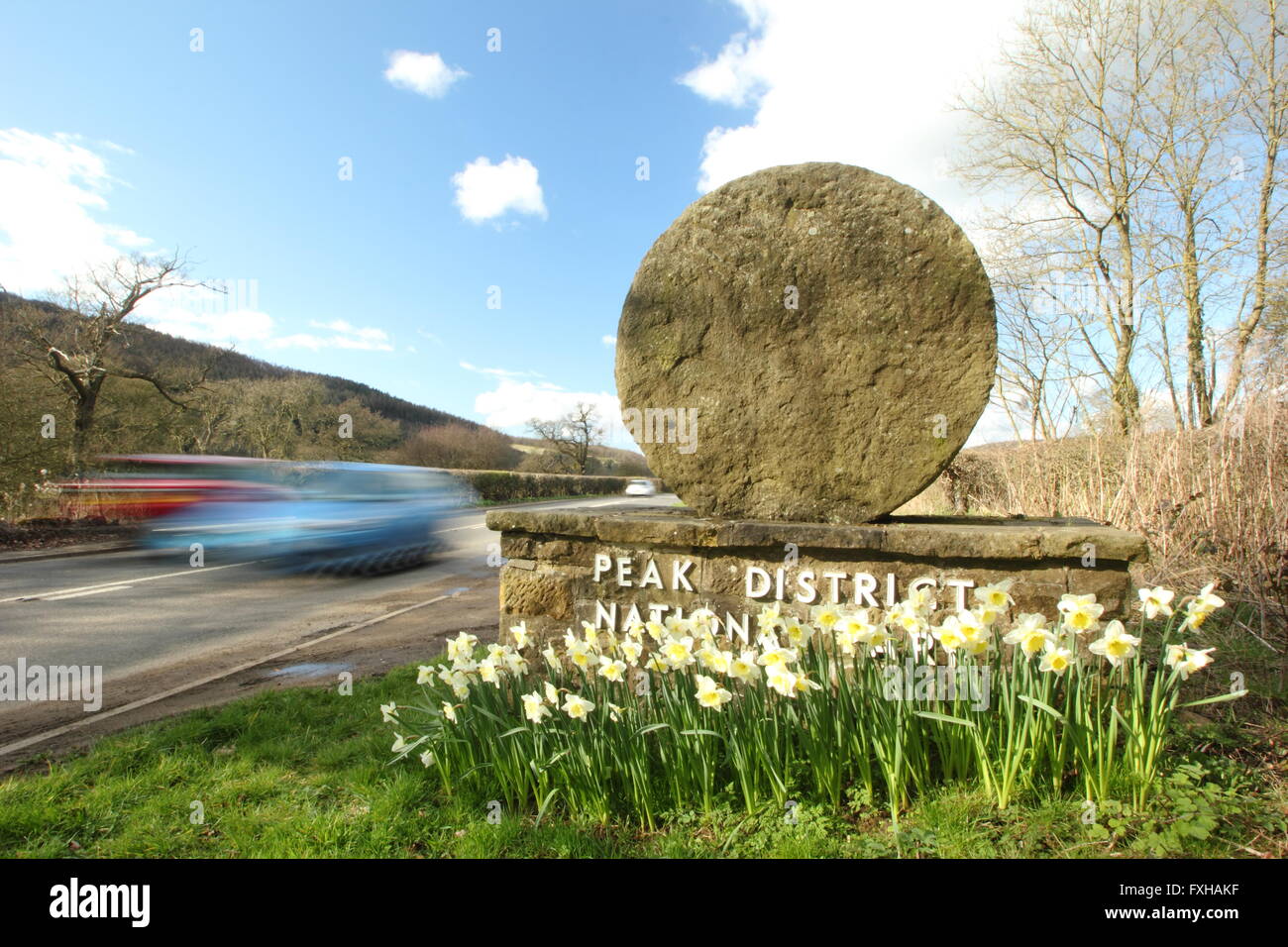 Autos fahren vorbei an einem Mühlstein Grenze Marker in der Peak District National Park, Derbyshire England UK - Frühling Stockfoto