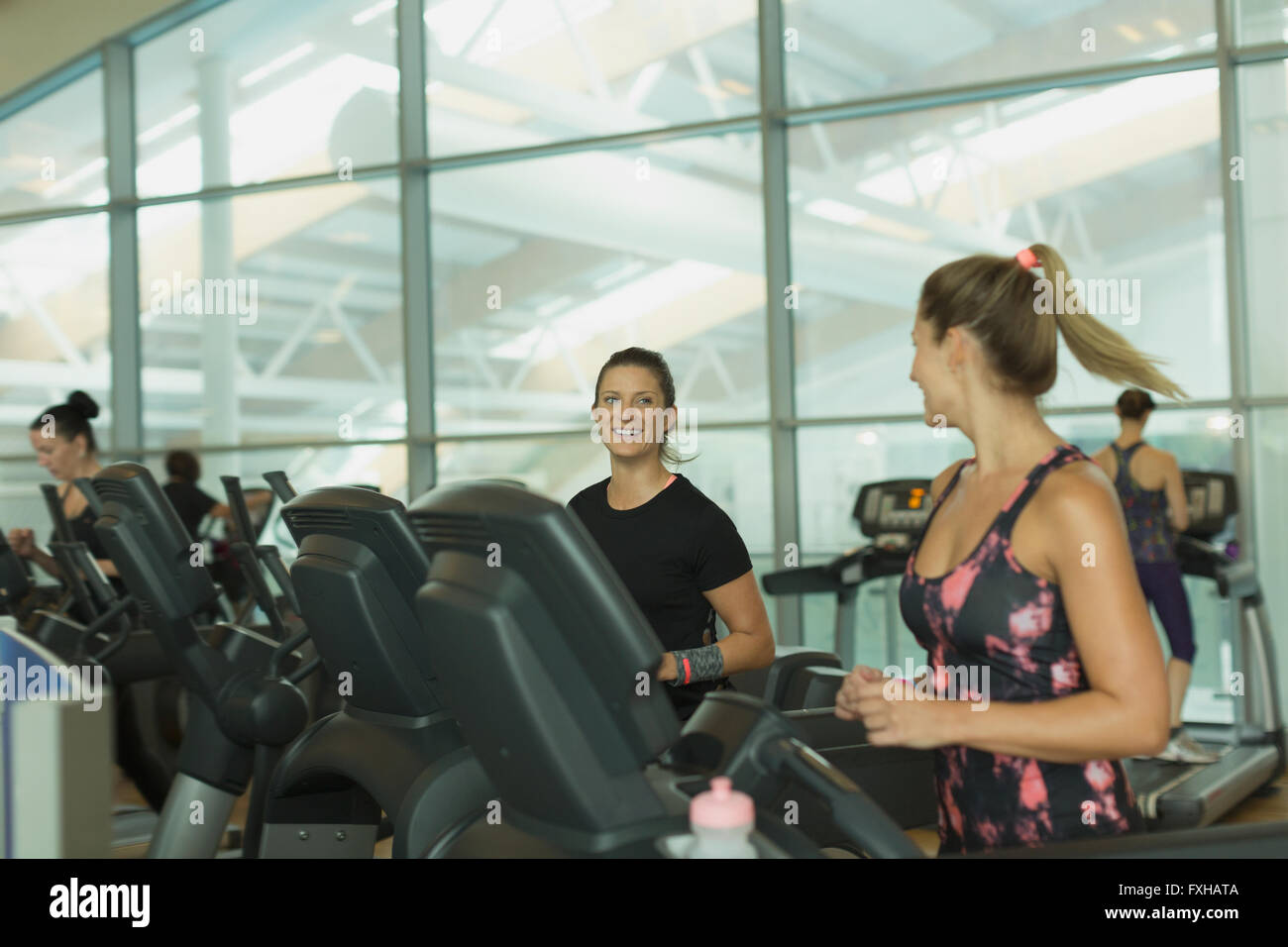 Lächelnde Frauen reden und Joggen auf dem Laufband im Fitnessstudio Stockfoto