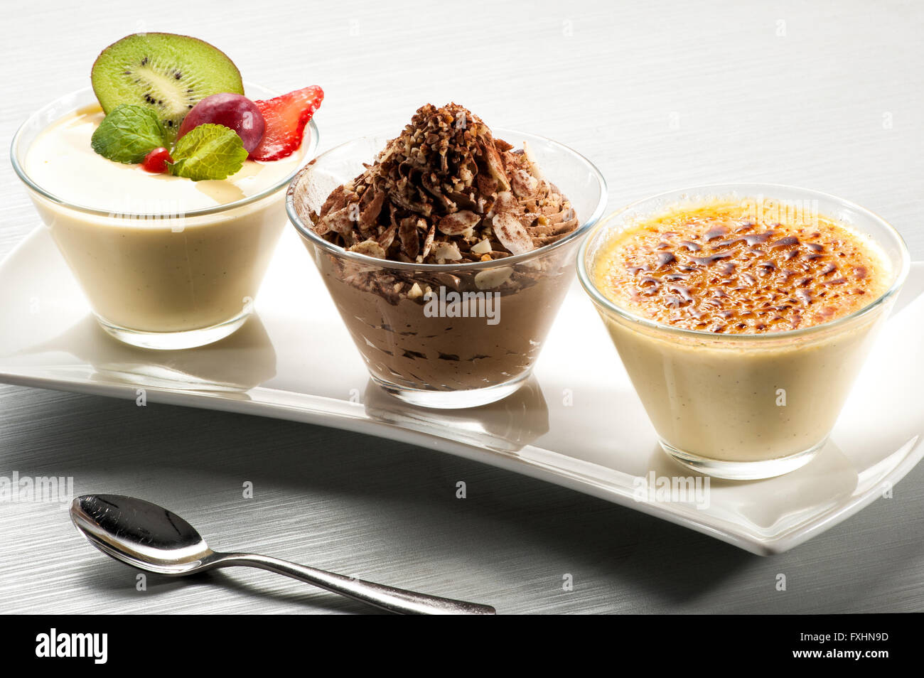 Elegant geschwungene Keramik glänzend Tablett mit drei kleinen Glasschalen mit Pudding, Schokolade und Vanille Obst gefüllt Stockfoto