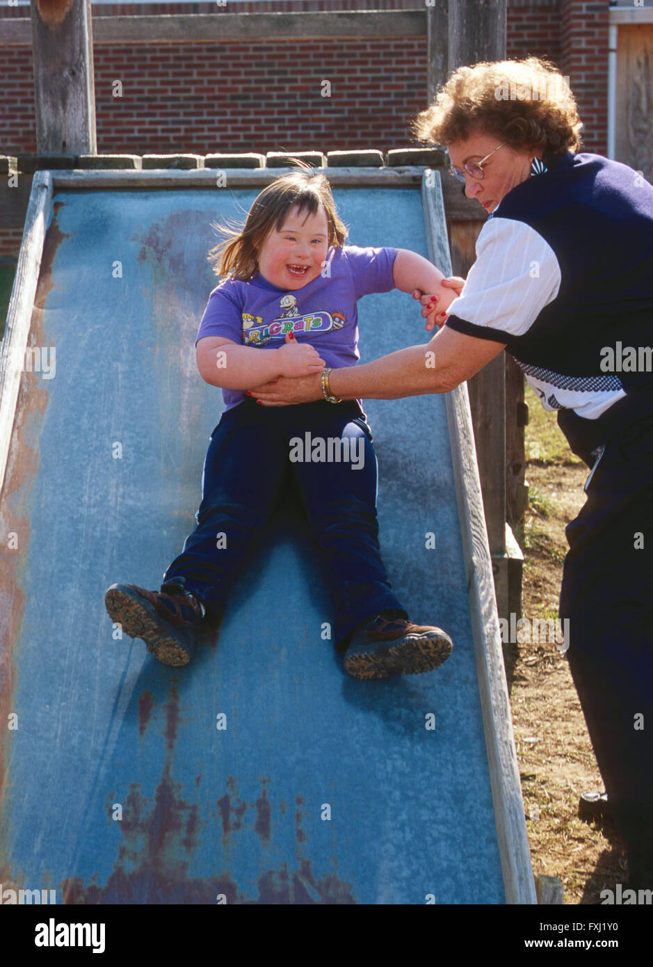 Lehrerin hilft behinderten Schüler auf die sliding board Stockfoto