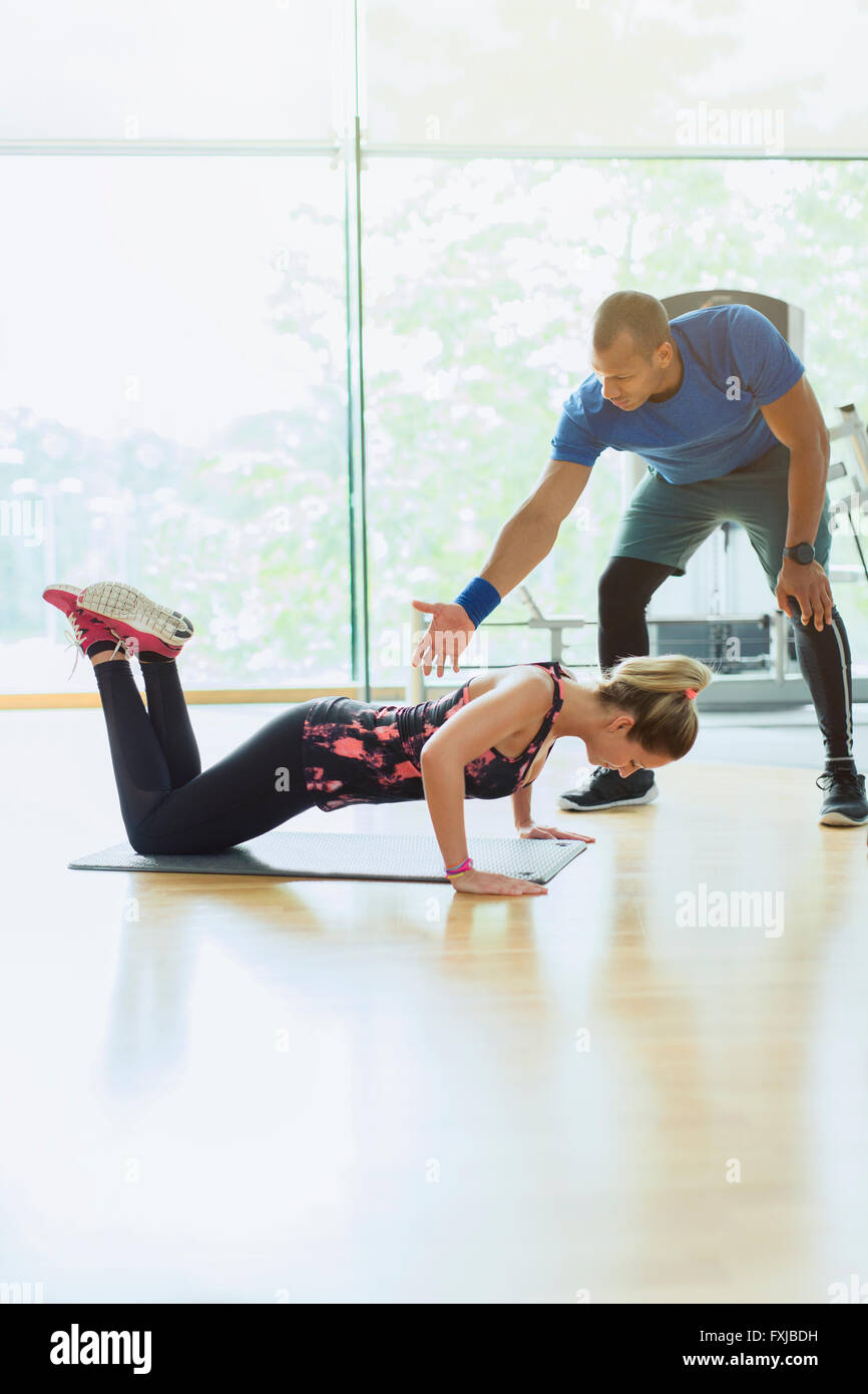 Persönlicher Trainer leiten Frau macht Liegestütze auf Knien beim Fitness-Studio Stockfoto
