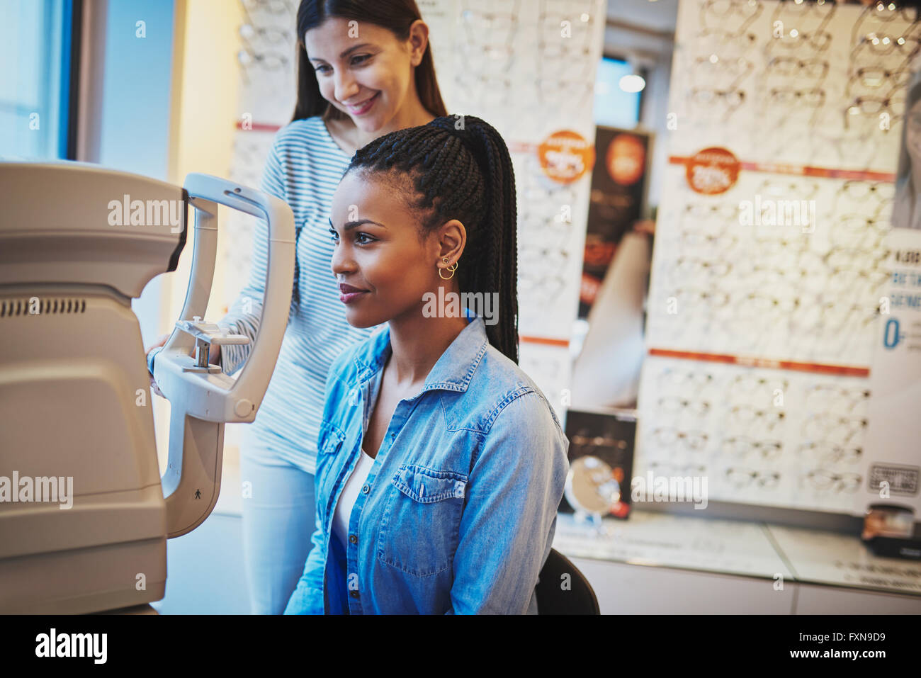 Schwere schwarze Frau mit Pferdeschwanz und trägt blaue Jean Shirt nimmt Eye Exam in optischen Shop Stockfoto