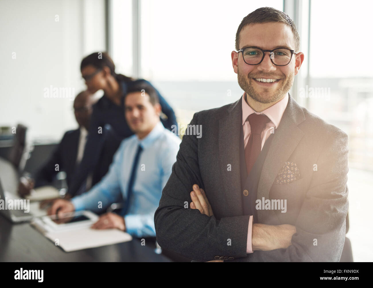 Zuversichtlich Lächeln Geschäftsmann mit verschränkten Armen in der Nähe von Konferenztisch mit drei Kollegen diskutieren etwas in großen Stockfoto