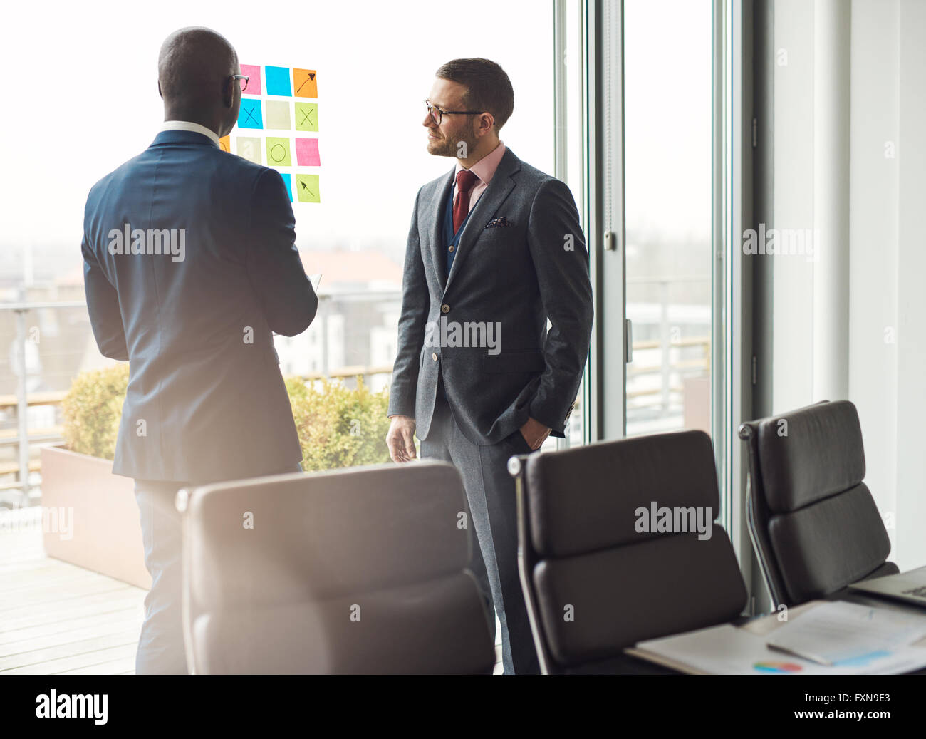 Zwei business Mann in stilvollen Anzügen stehen in einer Diskussion im Büro auf eine bunte Palette von klebrigen Memos auf dem Stockfoto