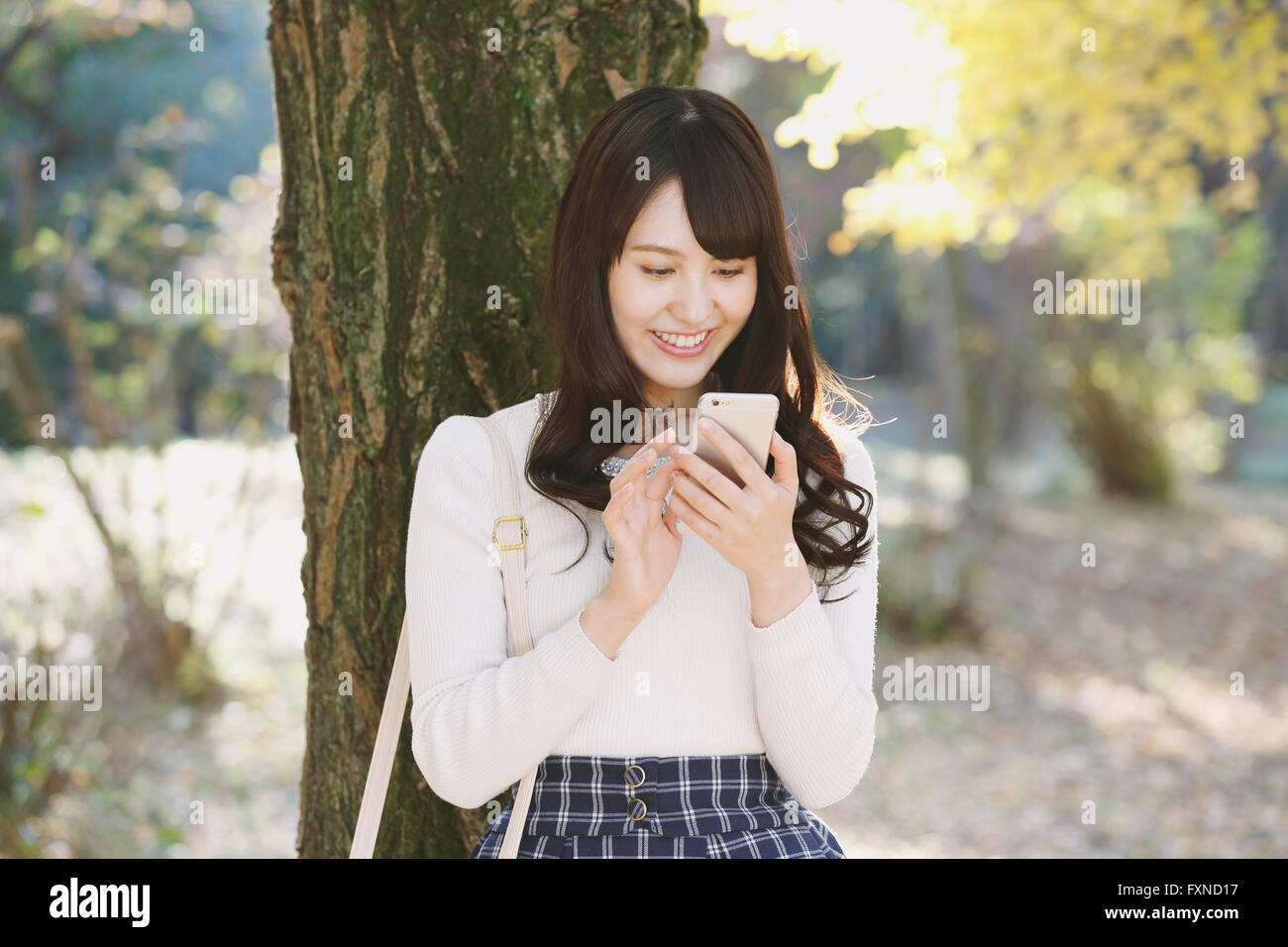 Junge Japanerin mit Smartphone in einem Stadtpark Stockfoto