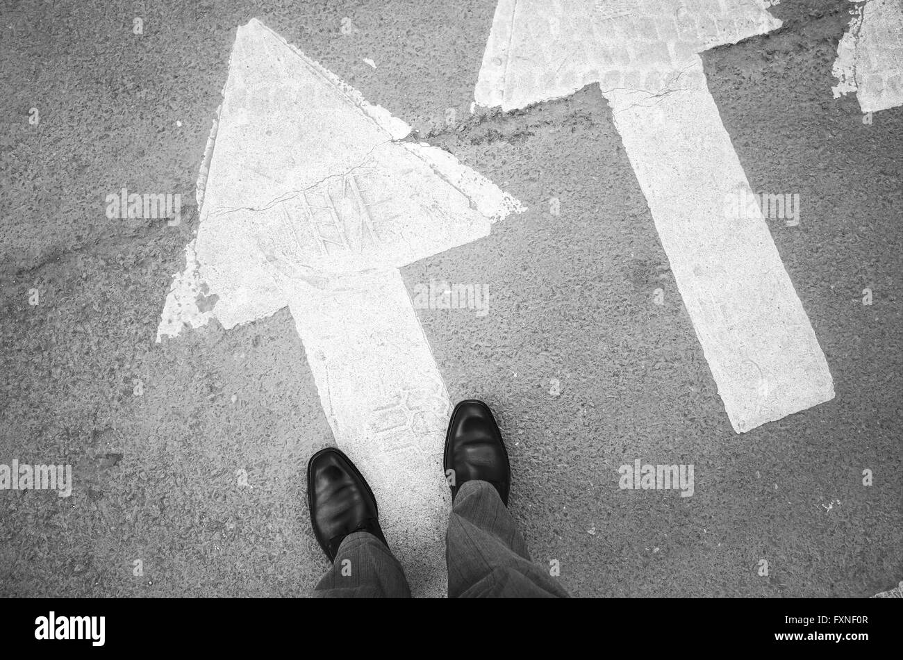 Männliche Füße in neuen schwarz glänzende Lederschuhe stehen auf Asphaltdecke mit weißen Pfeile Fußgängerüberweg Straßenmarkierung, zuerst Stockfoto