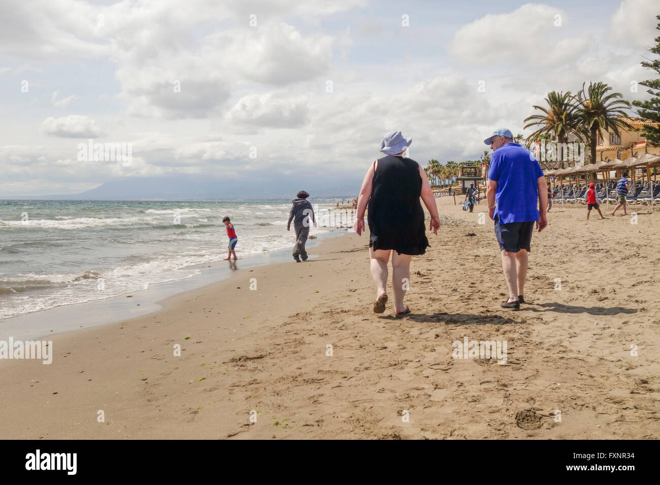 Älteres Ehepaar bei einem Spaziergang entlang des Strandes in Spanien, bei bewölktem Wetter. Andalusien, Spanien. Stockfoto