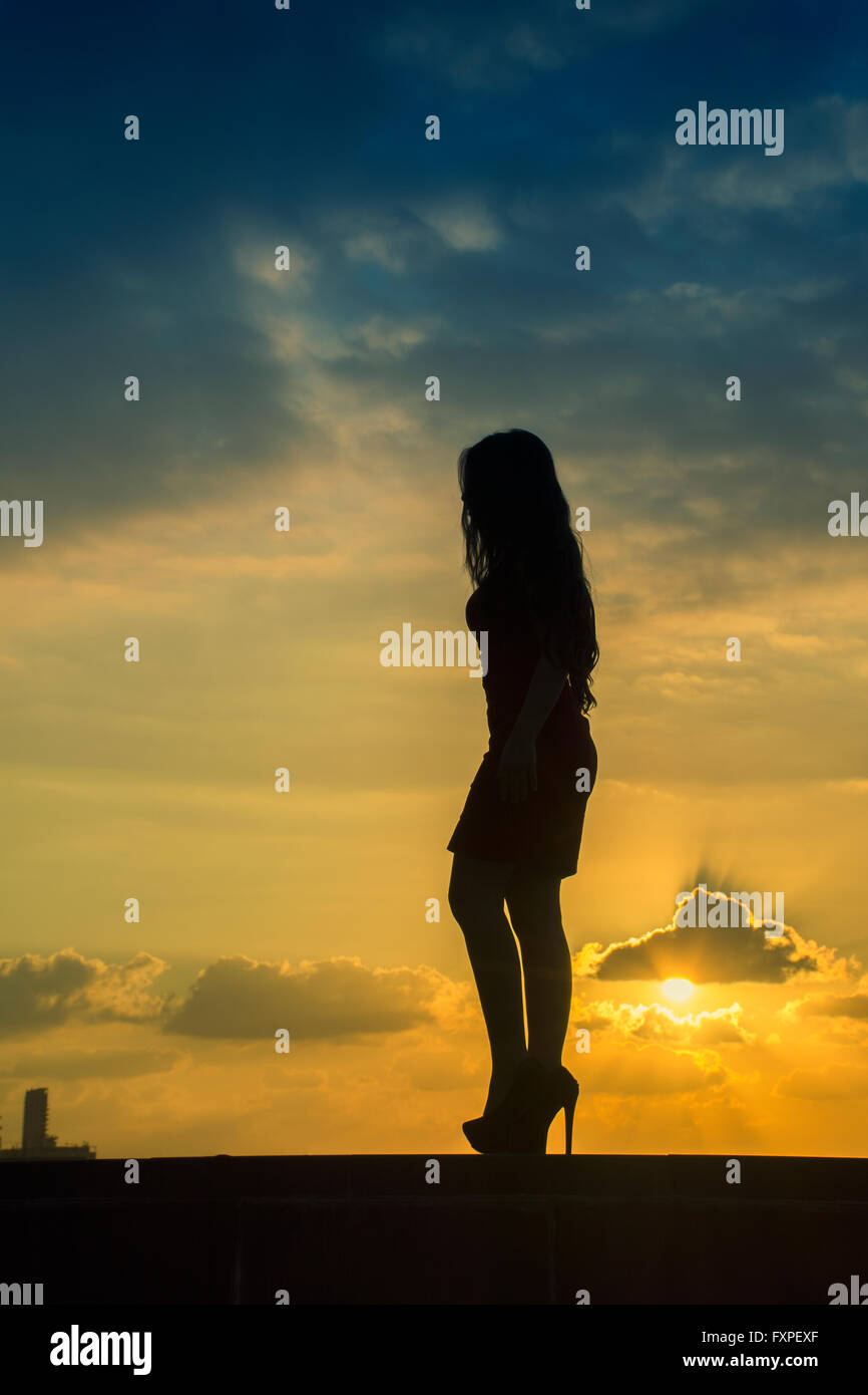 Volle Länge Frauen-Silhouette, die zu Fuß gegen einen dramatischen Sonnenuntergang Stockfoto