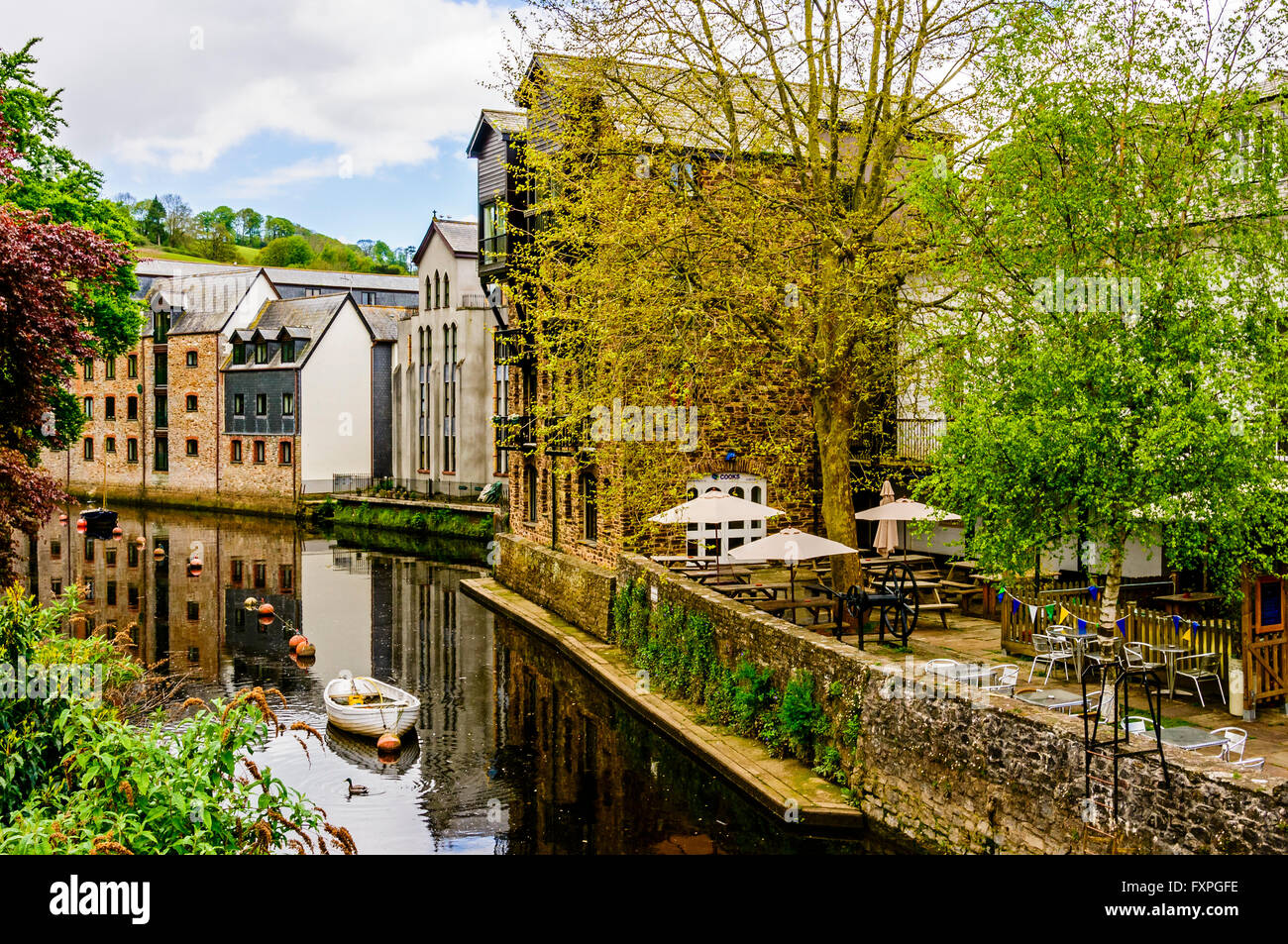 Boote vor Anker auf dem ruhigen Fluss Dart in Totnes zwischen renovierten alten Lagerhäusern auf der einen Seite und grüne Bäume auf der anderen Stockfoto