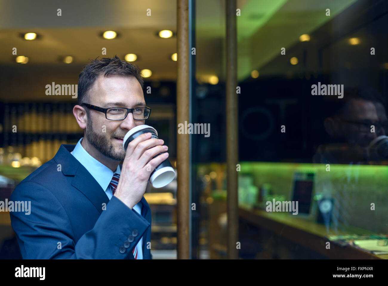 Bärtiger Mann mittleren Alters im blauen Anzug und Krawatte schlürfen Kaffee aus der Tasse in der Nähe von Tür bistro Stockfoto