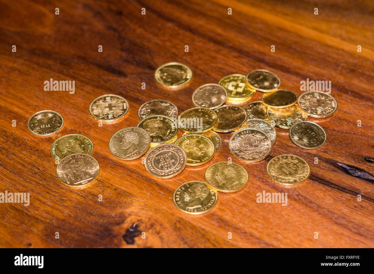 Mehrere Dutzend Goldmünzen, vor allem des 19. Jahrhunderts 20 Franken Münzen aus der Schweiz, gestapelt auf einem Holztisch. Stockfoto