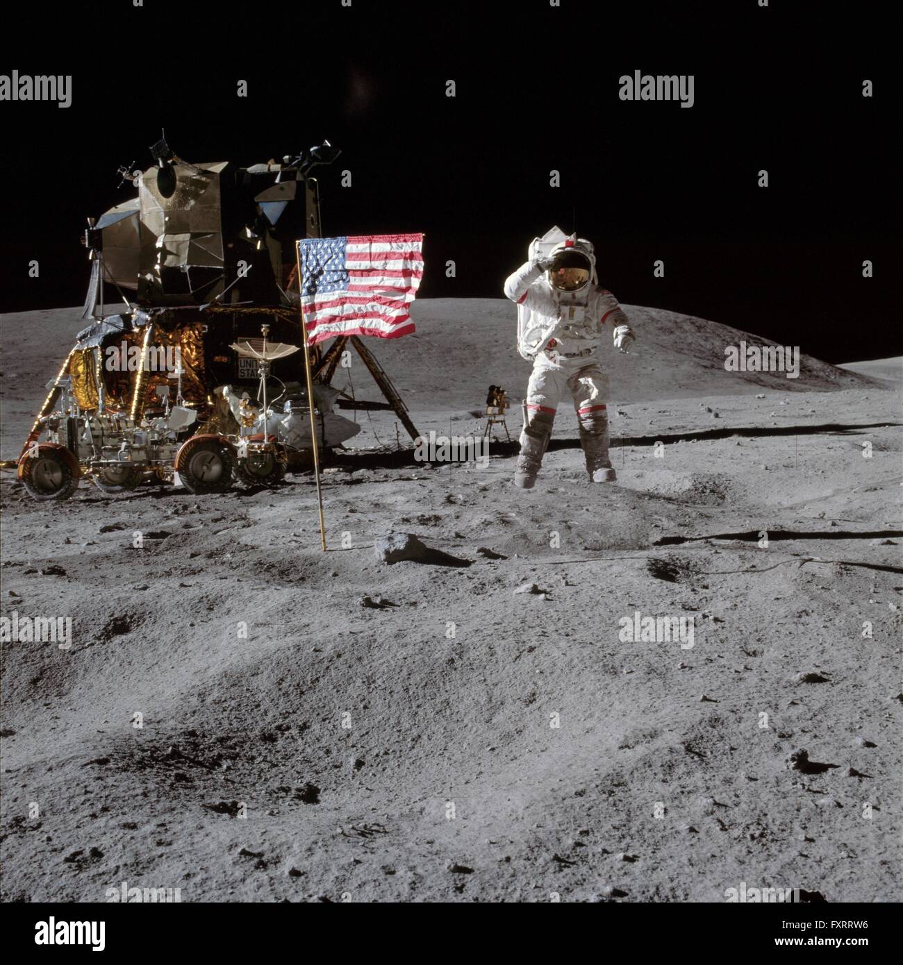 NASA-Astronauten und Apollo 16 Kommandant John W. Young springt von der Mondoberfläche als He grüßt die Flagge der Vereinigten Staaten am Landeplatz Descartes während der ersten EVA-Mission 21. April 1972. Die Mondlandefähre Orion und die Lunar Roving Vehicle sind jungen links. Stockfoto