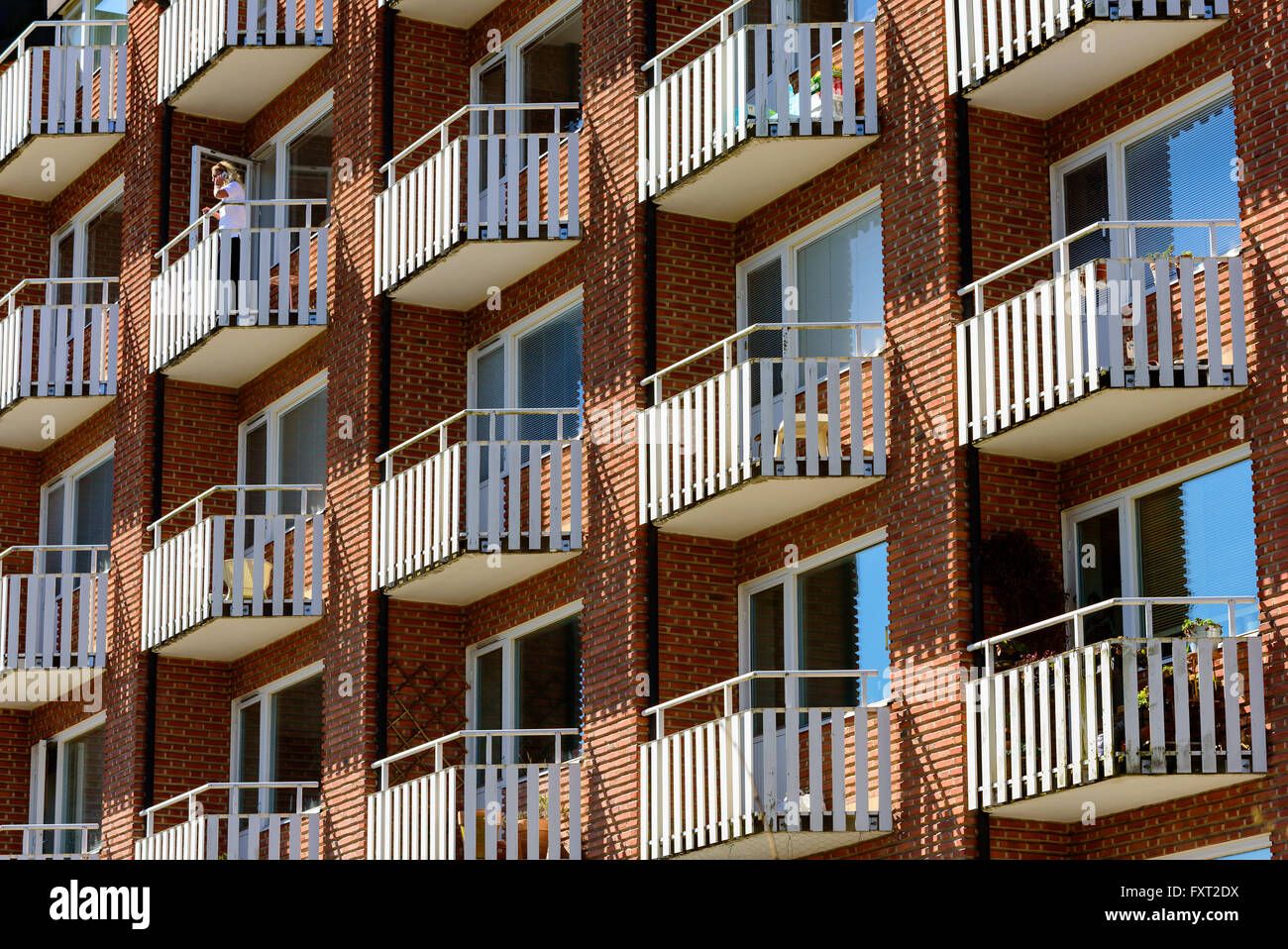 Lund, Schweden - 11. April 2016: Weißen Balkonen auf einem roten Backsteingebäude in der Stadt. Frau im Gespräch im Telefon auf einem Balkon. Stockfoto