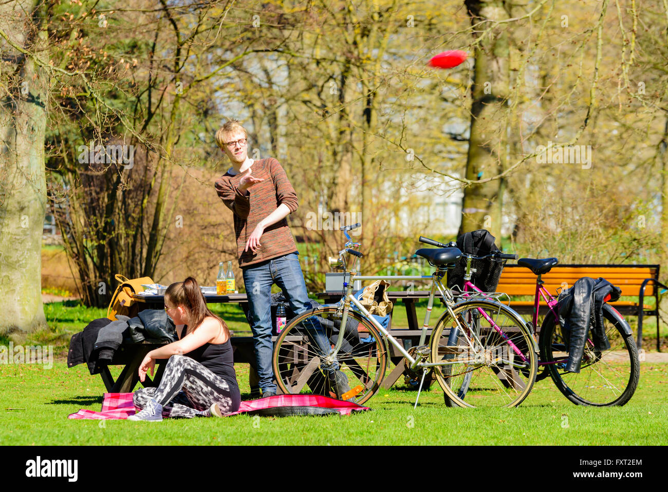 Lund, Schweden - 11. April 2016: Leben in der Stadt jeden Tag. Jungen Erwachsenen Mannes in einem Park ist eine fliegende Scheibe werfen, während eine Frau her in sitzt Stockfoto