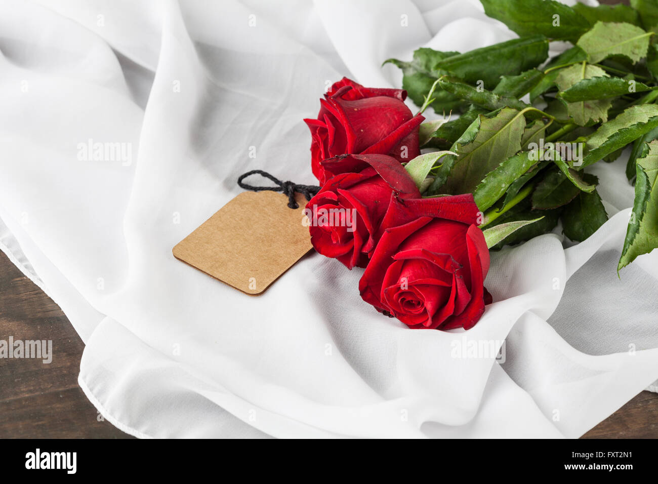 Drei rote Rosen mit Geschenk-Tag auf Seide Falten mit Textfreiraum. Elegante Frauen Tag anwesend. Geringe Schärfentiefe Stockfoto