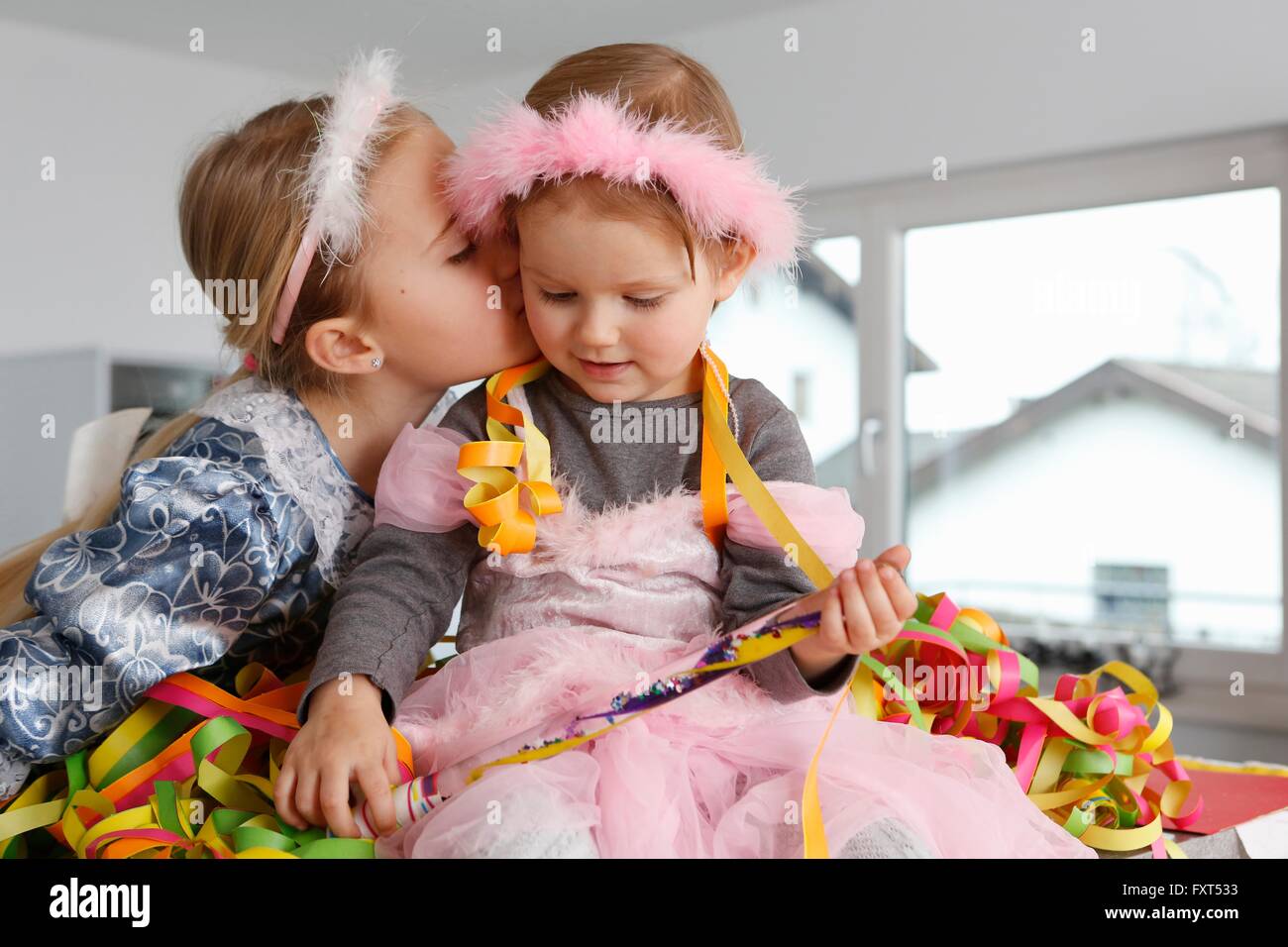 Schwestern verkleidet als Prinzessinnen, bedeckt in Partystromern, Kuss auf Wange Stockfoto