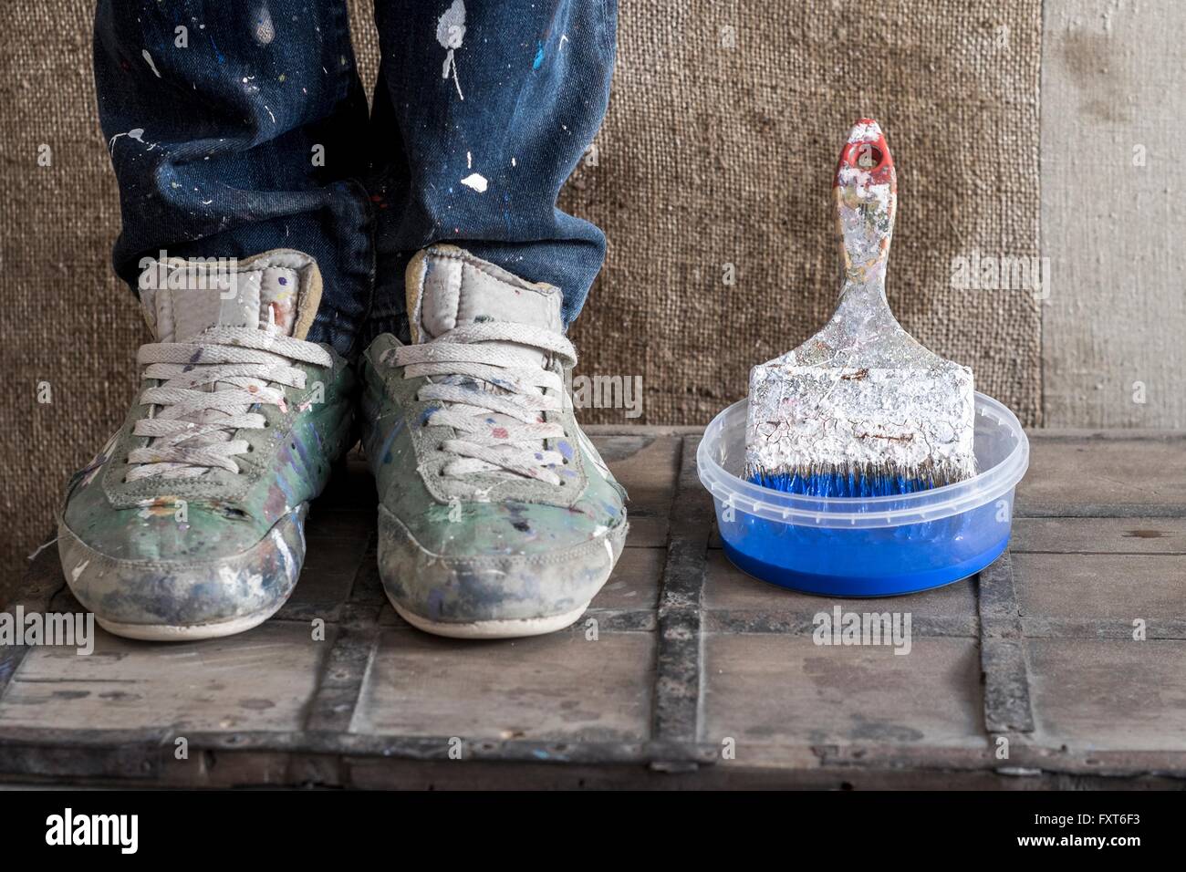 Beine mit schmutzigen Schuhen neben Kunststoff-Behälter mit Pinsel Stockfoto