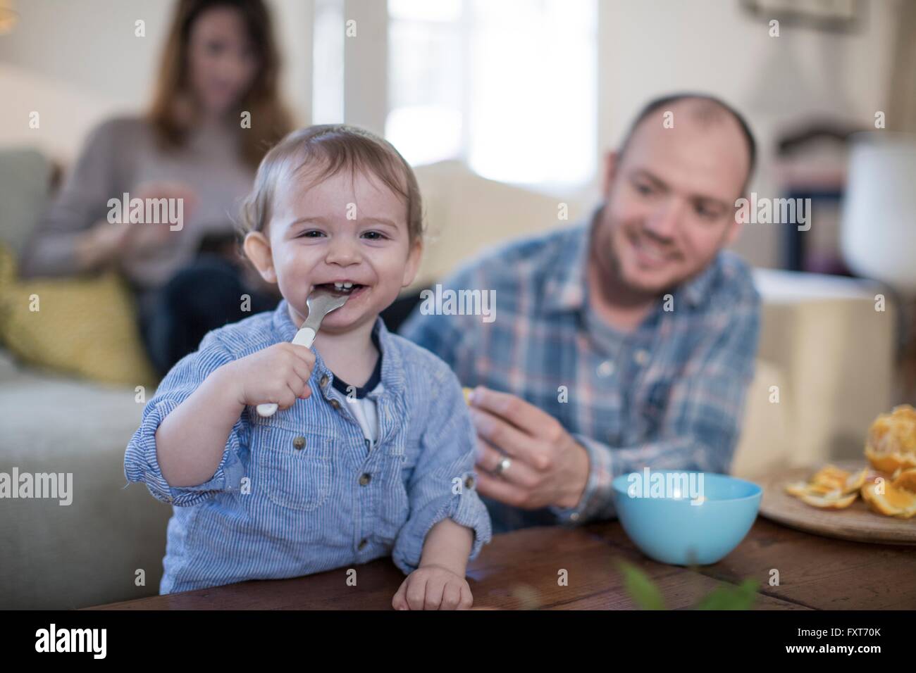 Baby Boy Fütterung selbst mit Löffel, Blick auf die Kamera zu Lächeln Stockfoto