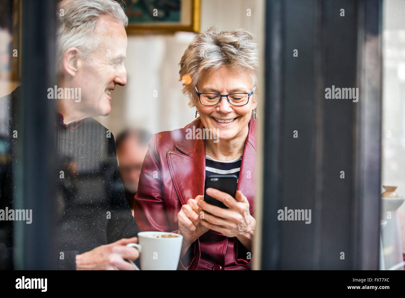 Älteres Paar sitzt am Fensterplatz Café trinken Kaffee und SMS auf dem smartphone Stockfoto