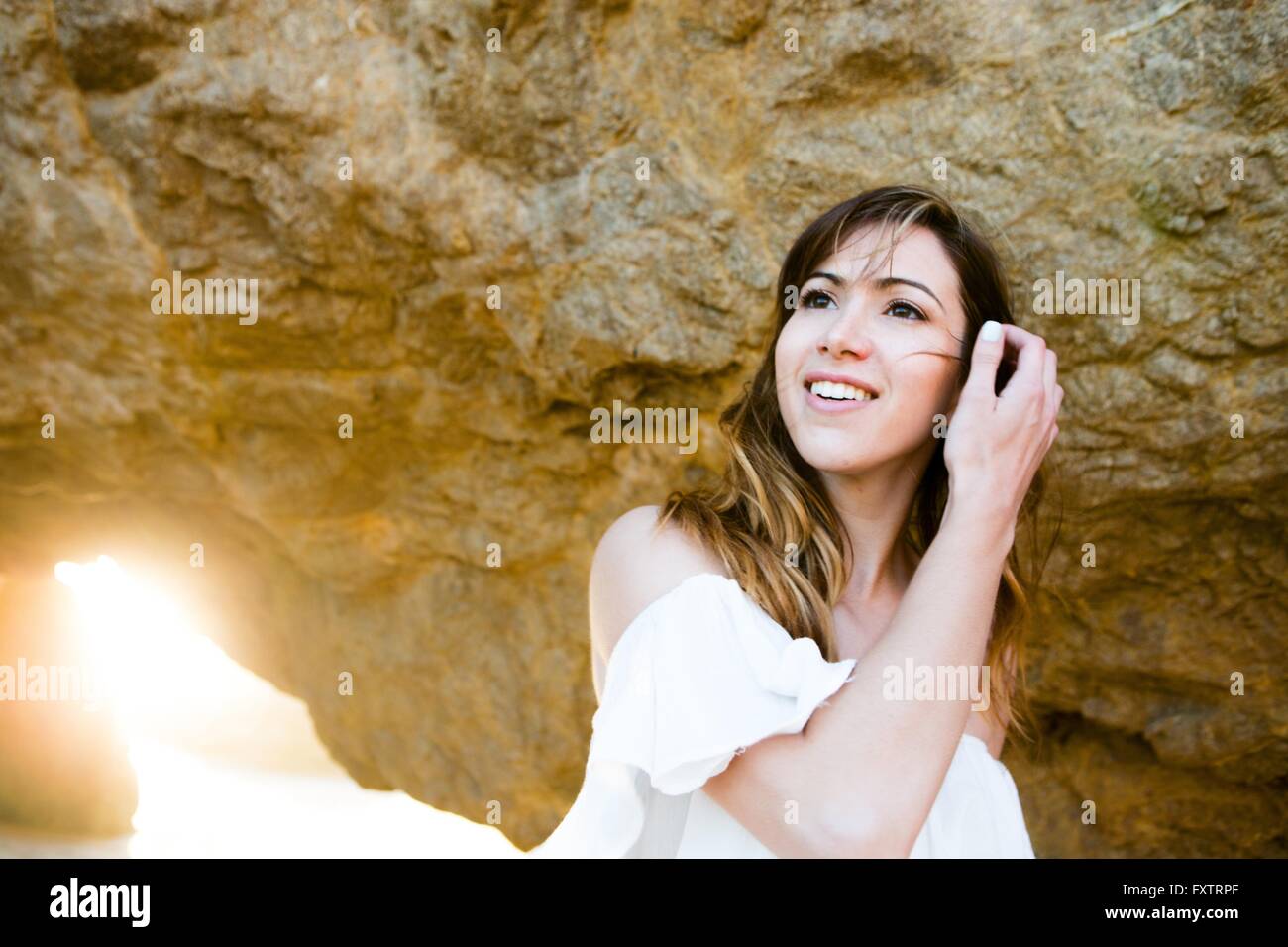 Junge Frau, die Haare hinter Felsformation aufräumen Stockfoto