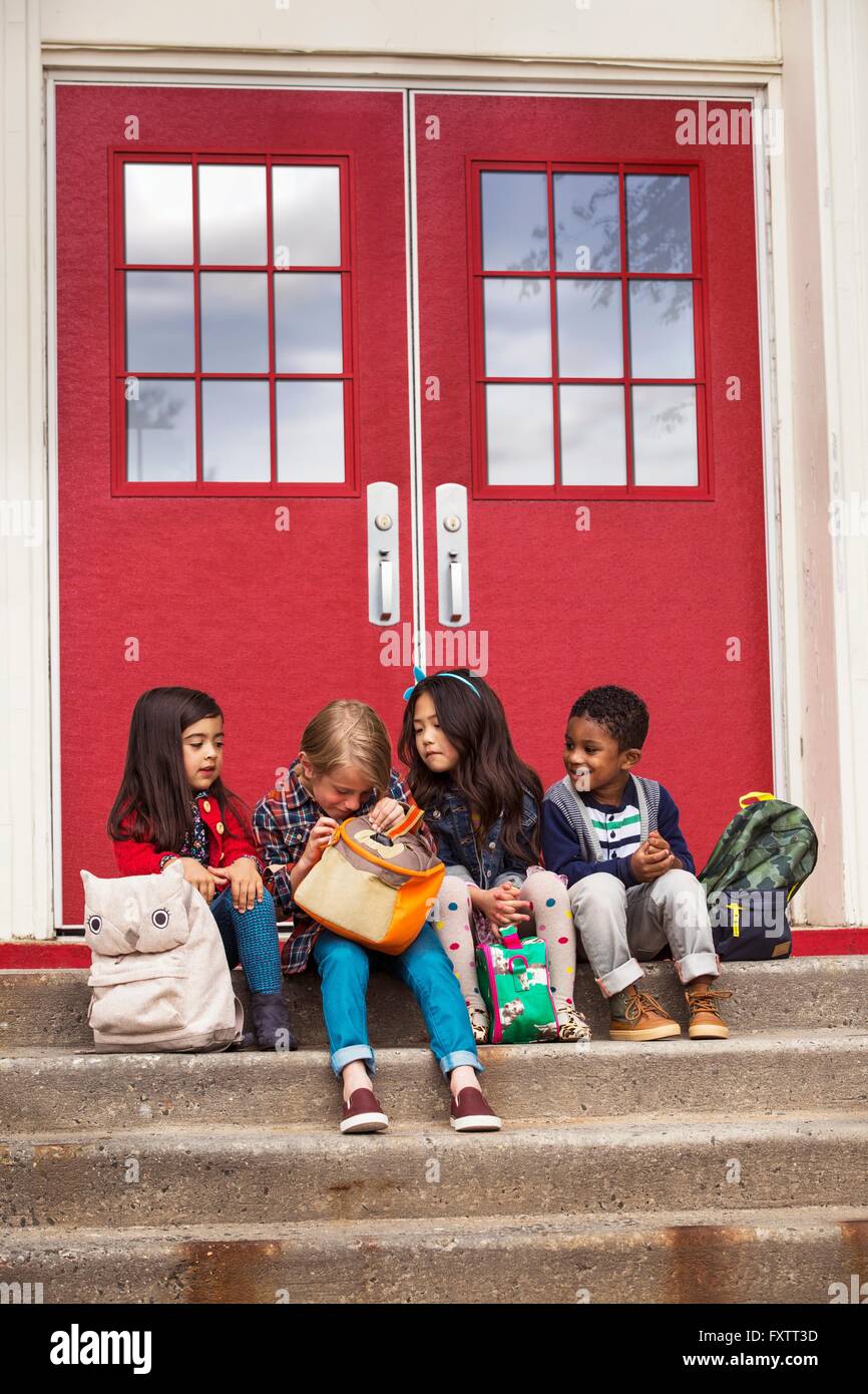 Elementare Schülerinnen und jungen sitzen auf Grundschule Tür Treppe im Schulranzen Stockfoto
