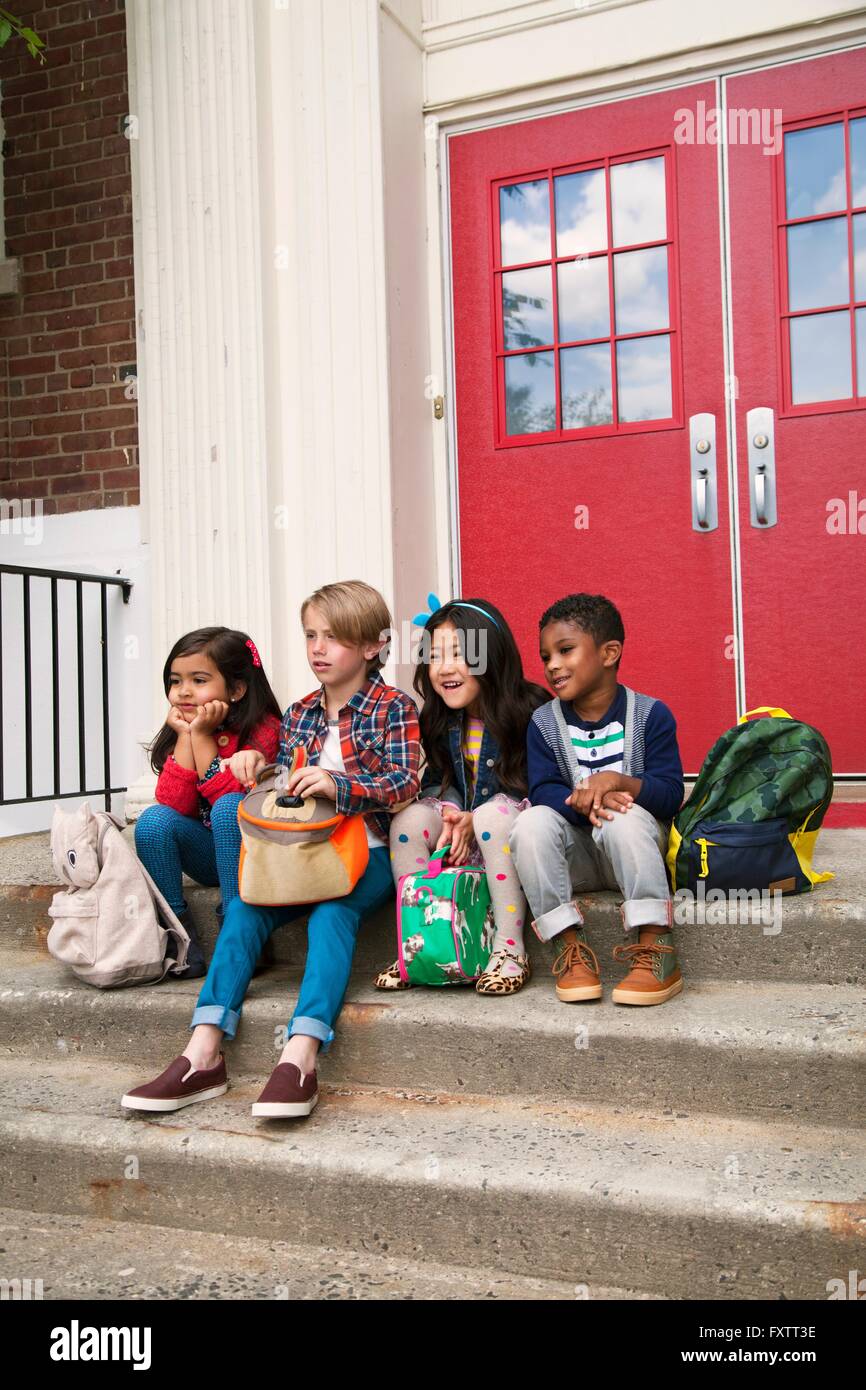 Elementare Schülerinnen und jungen sitzen auf Grundschule Tür Treppe Stockfoto
