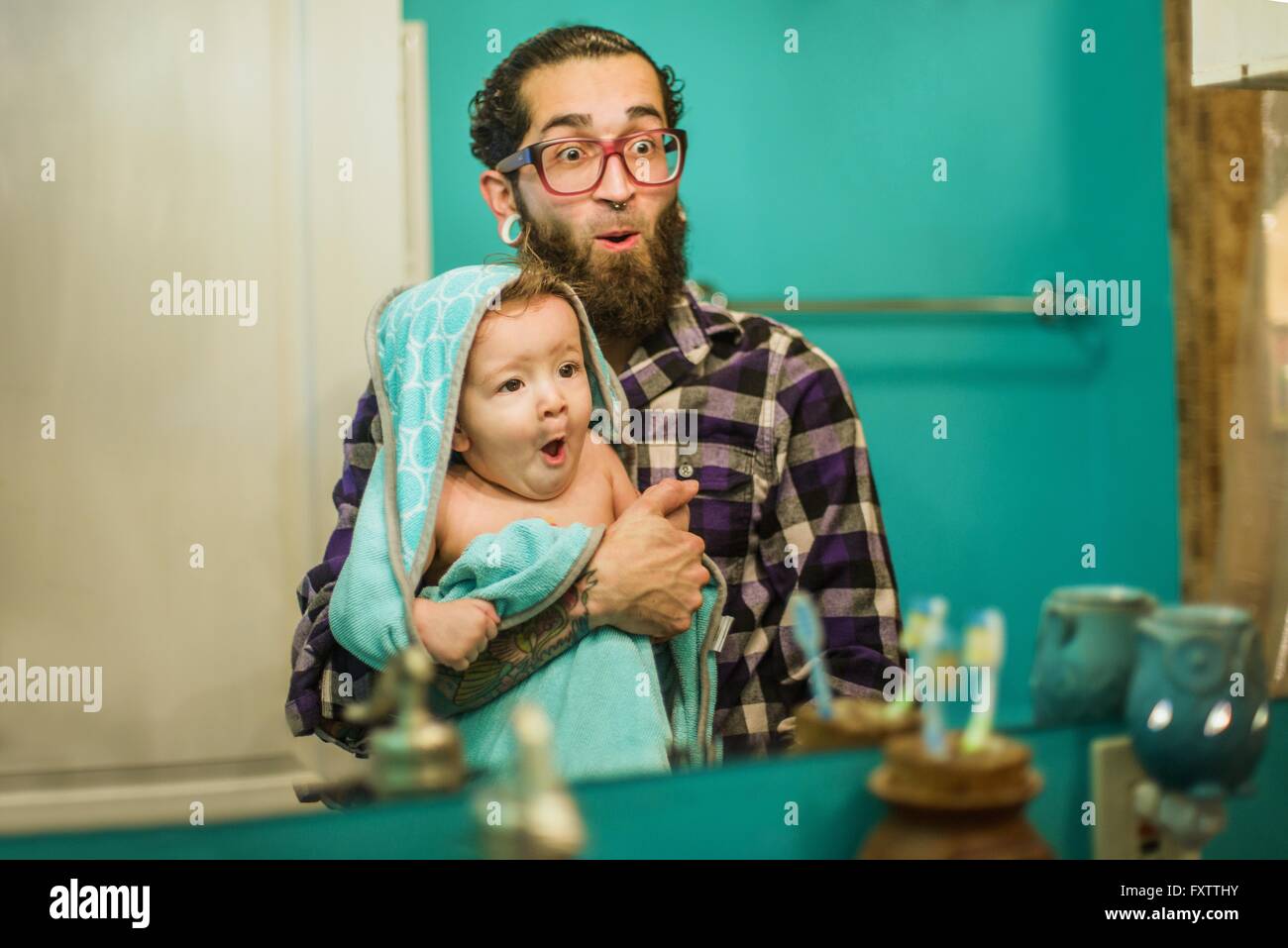 Spiegelbild der junge Mann und Baby Sohn Grimassen im Badezimmer Stockfoto