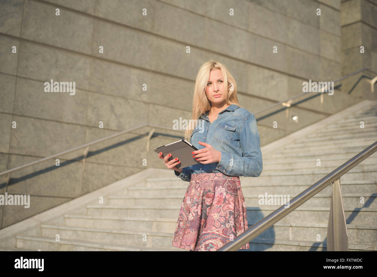 Online verbunden Knie Abbildung der junge schöne blonde kaukasische Mädchen mit einem Tablet auf einer Treppe in der Stadt trug Jeans Hemd und floralen Rock - Technologie, Kommunikation, soziale Netzwerk-Konzept Stockfoto