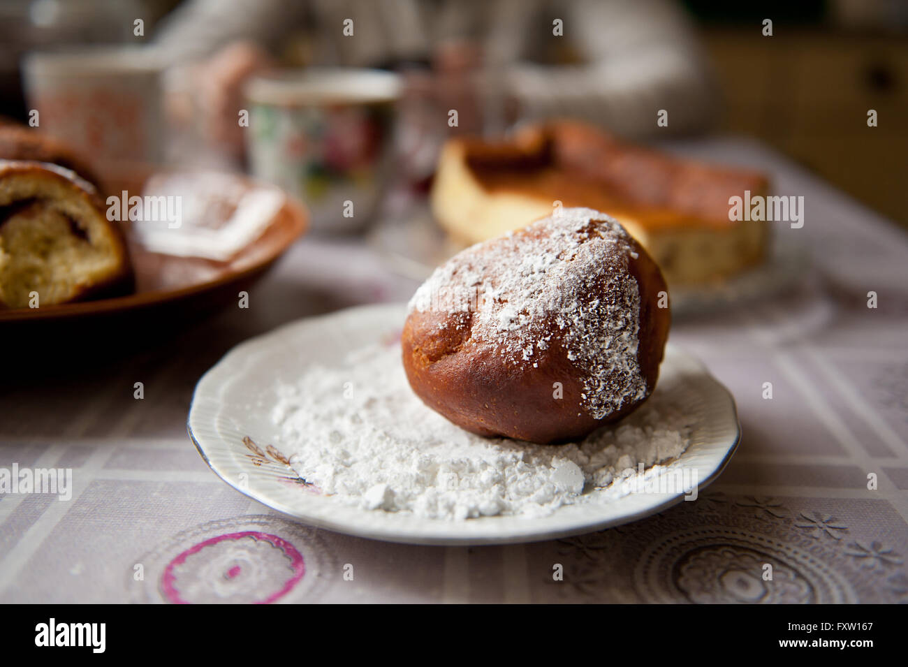 Fettiger Donut auf Puderzucker auf Platte auf dem Küchentisch liegend mit Wachstuch, große leckere hausgemachte Krapfen süß gebraten Stockfoto