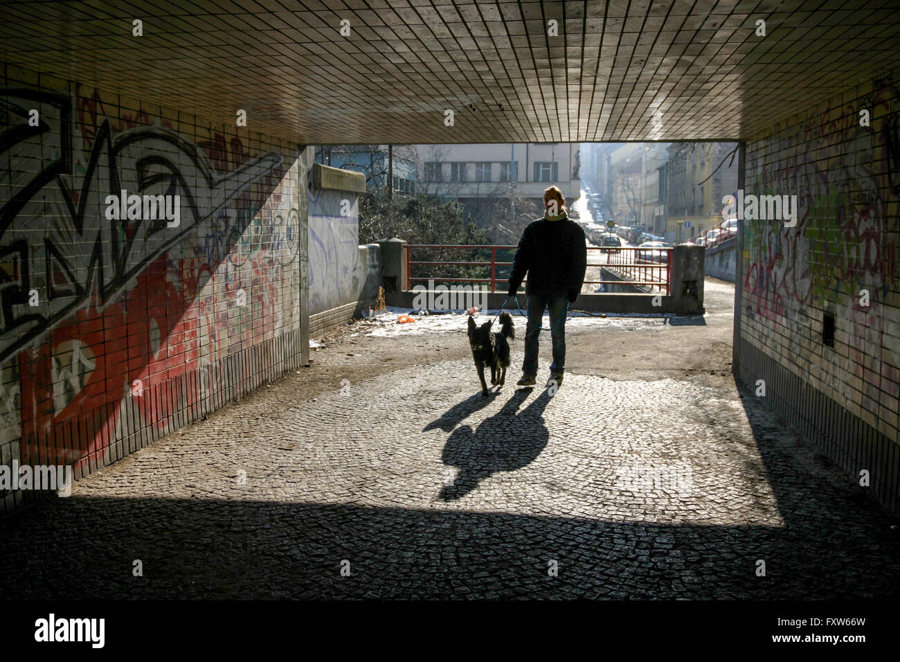 Ein Mann mit einem Hund ein Spaziergang, unterquert Prag Zizkov Mann und Hund gehen allein in einer städtischen Szene im Hintergrund, Silhouette mit Schatten auf dem Boden Stockfoto