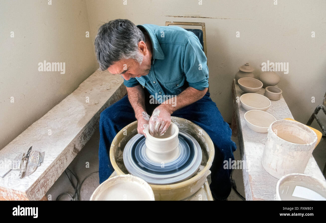 Eine Töpferscheibe dreht mit Ton, während der Künstler seine nassen Händen verwendet, um eine Keramikschale zu gestalten, die später in einem Brennofen zu den fertigen Topf Härten ausgelöst wird. Die hohe Temperatur im Ofen verdunstet das Wasser aus der Tongefäße, so dass die Schale seine Form behält. Dieser männliche Potter ist in seiner eigenen Werkstatt in Sonoma, Kalifornien, USA. Auf einer der Holzbänke sind weitere Töpfe, er hat an diesem Tag geworfen und sind bereit für den Brennofen. -Modell veröffentlicht. Stockfoto