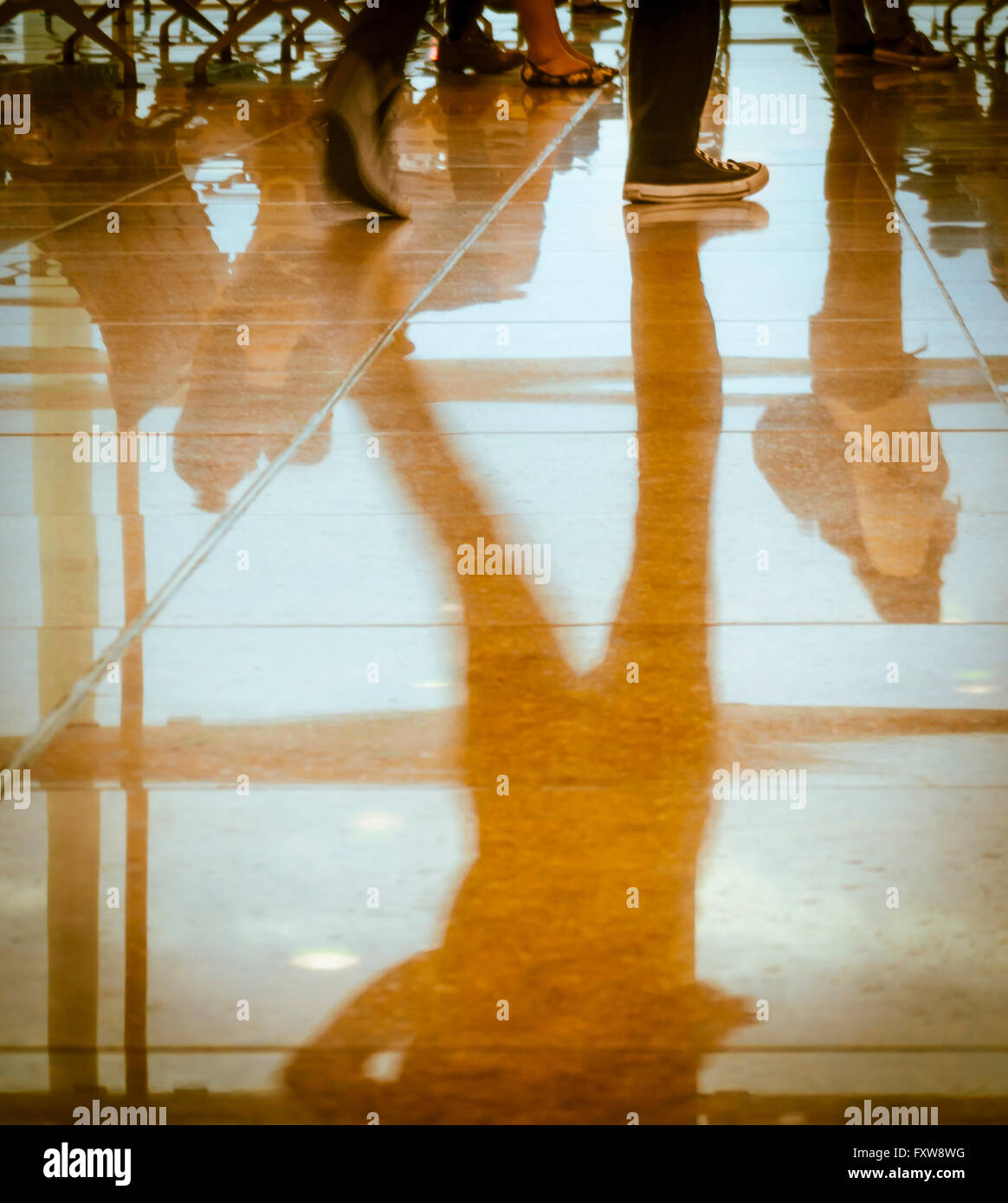 Reflexionen von Silhouetten der Beine, Füße und unteren Körperteile der Geschäftsreisende auf einem Flughafen /station Halle. Warme Farben. Stockfoto