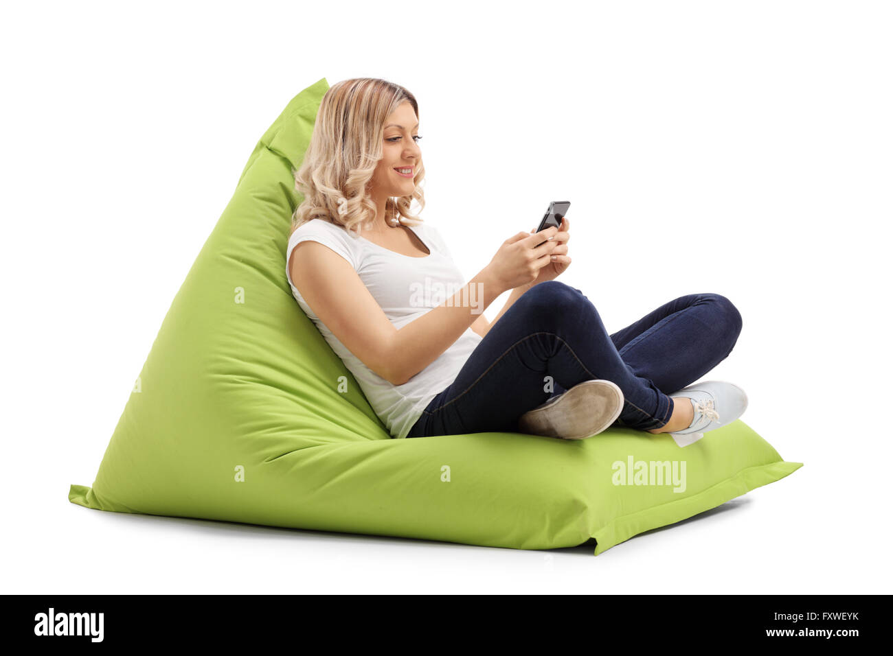 Blonde Frau, die SMS auf ihrem Handy sitzt auf einer grünen Sitzsack isoliert auf weißem Hintergrund Stockfoto