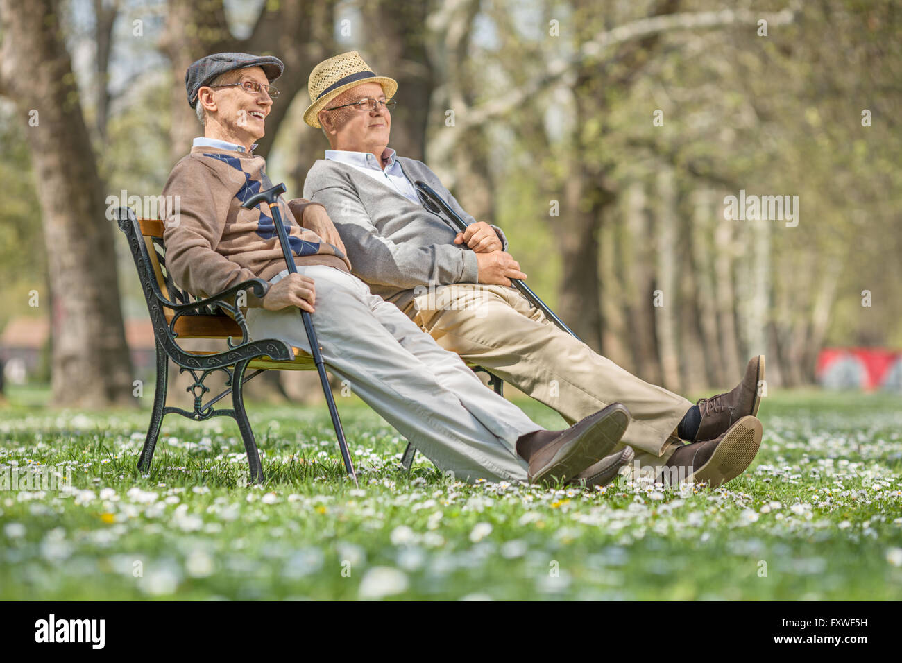 Zwei ältere Herren sitzen und entspannen auf einer Holzbank in einem Park an einem sonnigen Tag Stockfoto