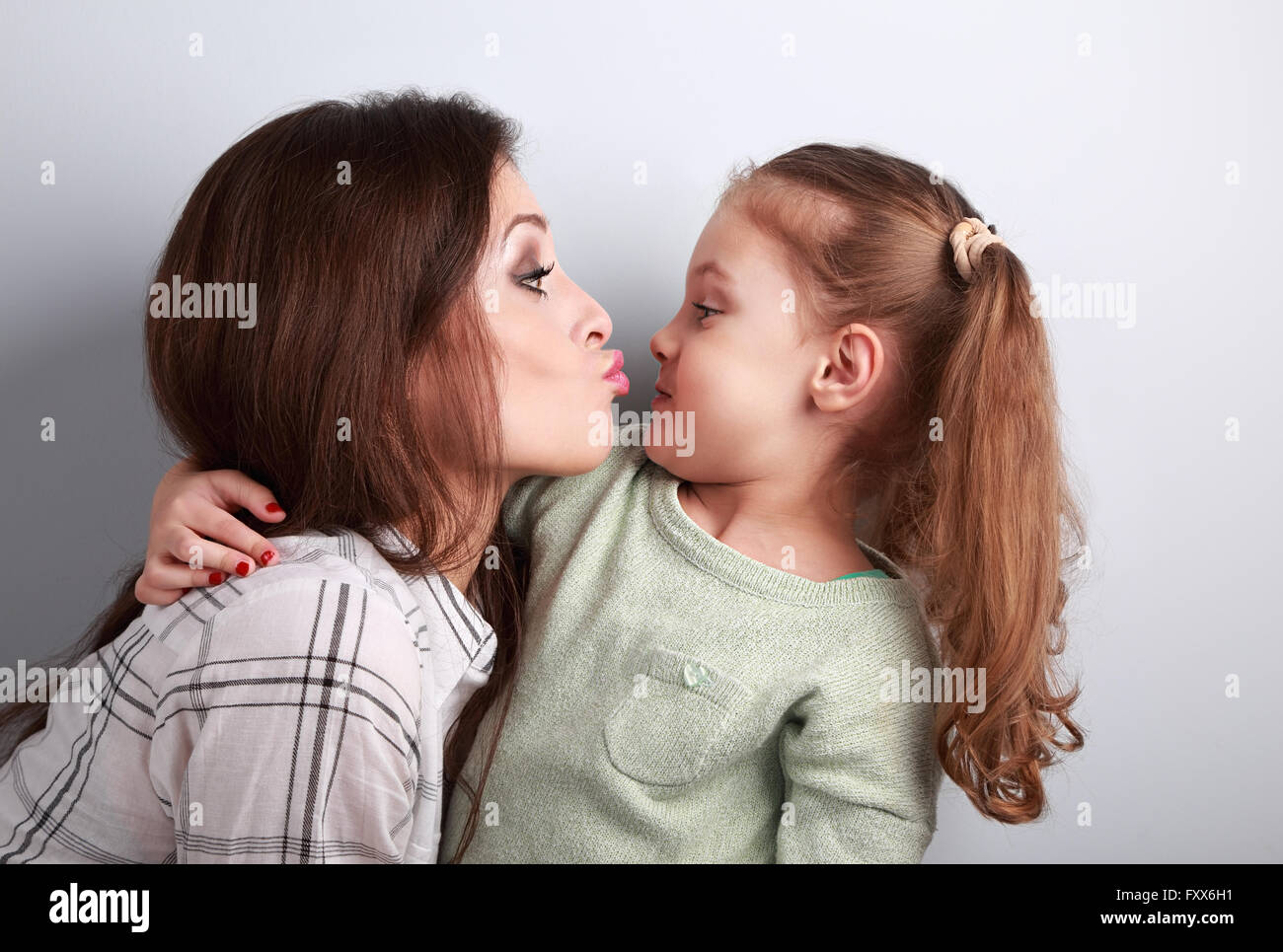 Lustige lustige junge Mutter ihre komischen grimassierende Tochter im Studio küssen wollen Stockfoto