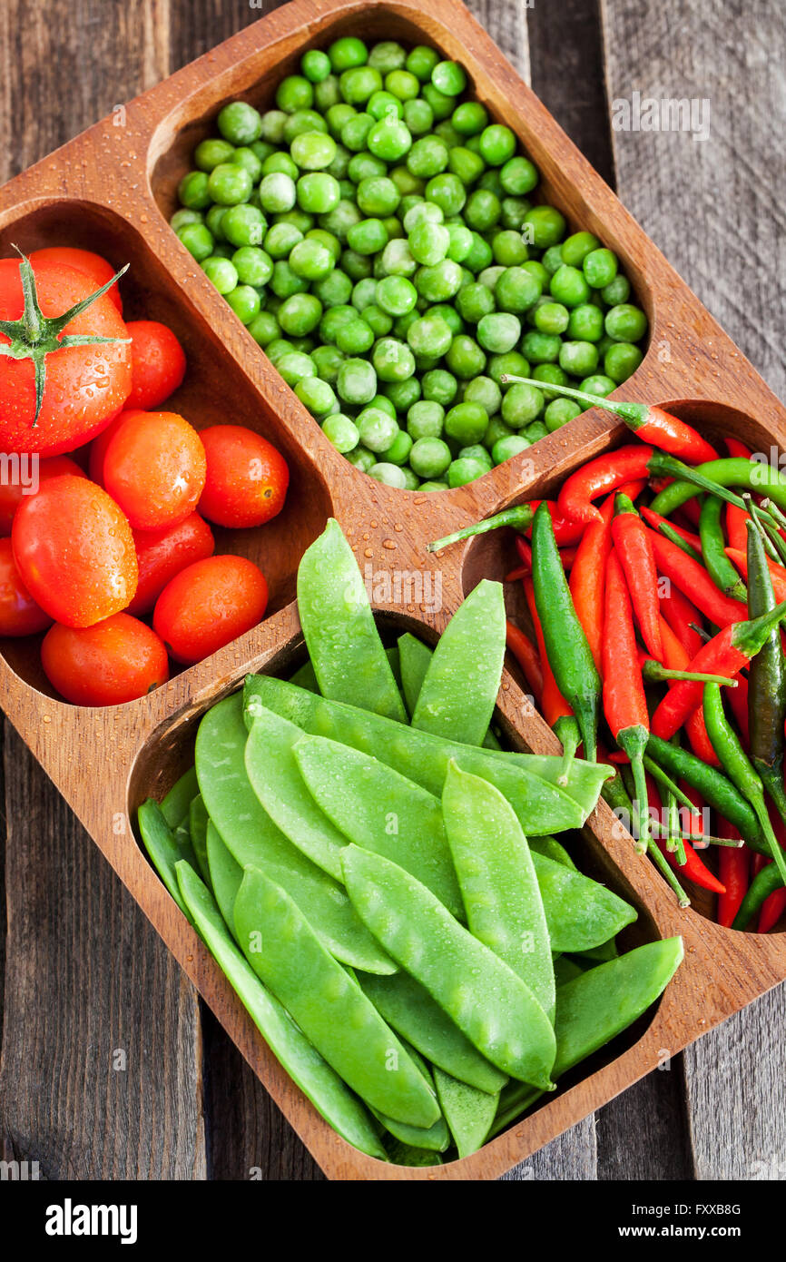Frische grüne Erbsen, Tomaten und Paprika in Holzschale Stockfoto