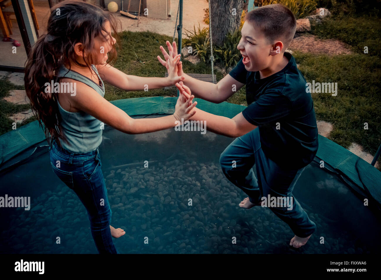 Zwei Kinder (junge und Mädchen) beim Springen auf dem Trampolin und lachend durch die Luft fliegen Stockfoto