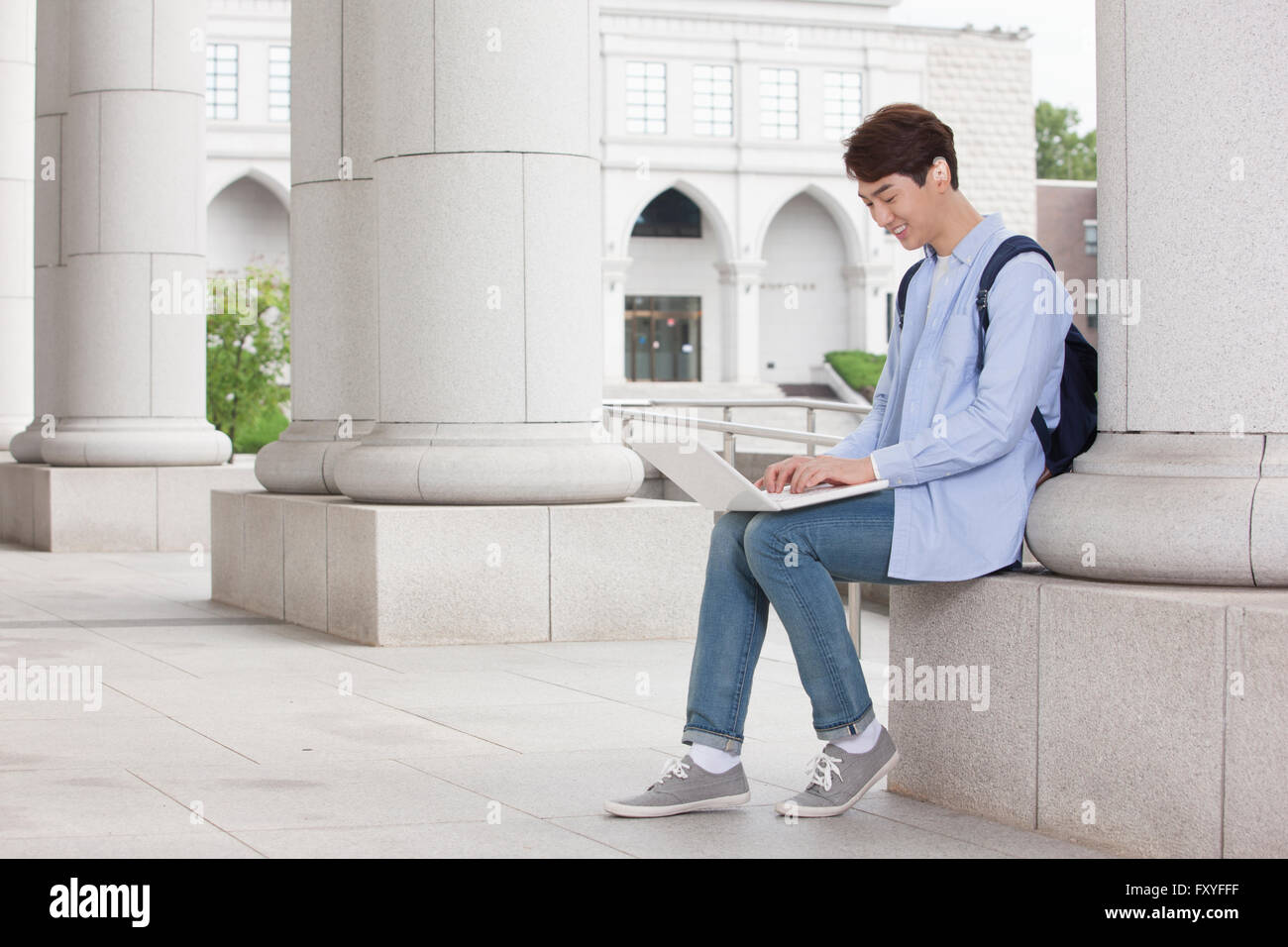 Junge College in einer Spalte eines Campus Gebäude und arbeitet an seinem Laptop sitzt Stockfoto
