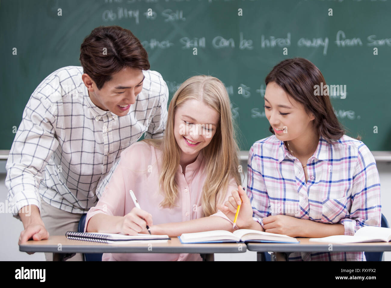 Zwei einheimische Studierende, die einen internationalen Student mit dem Studium in einem Klassenzimmer in der Schule helfen Stockfoto