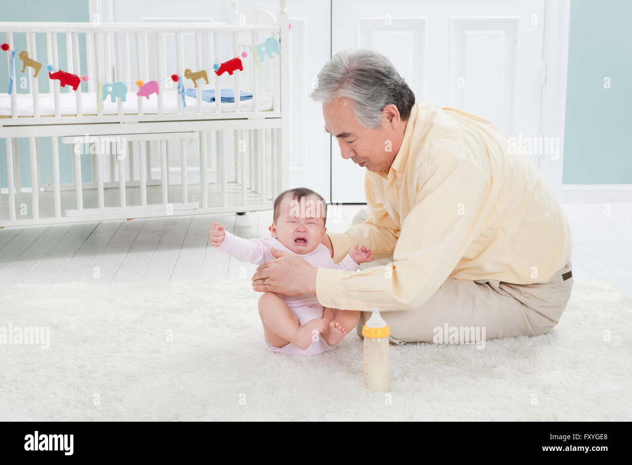 Ältere Mann kümmert sich um ein schreiendes Baby, die, das beide auf dem Boden sitzend Stockfoto